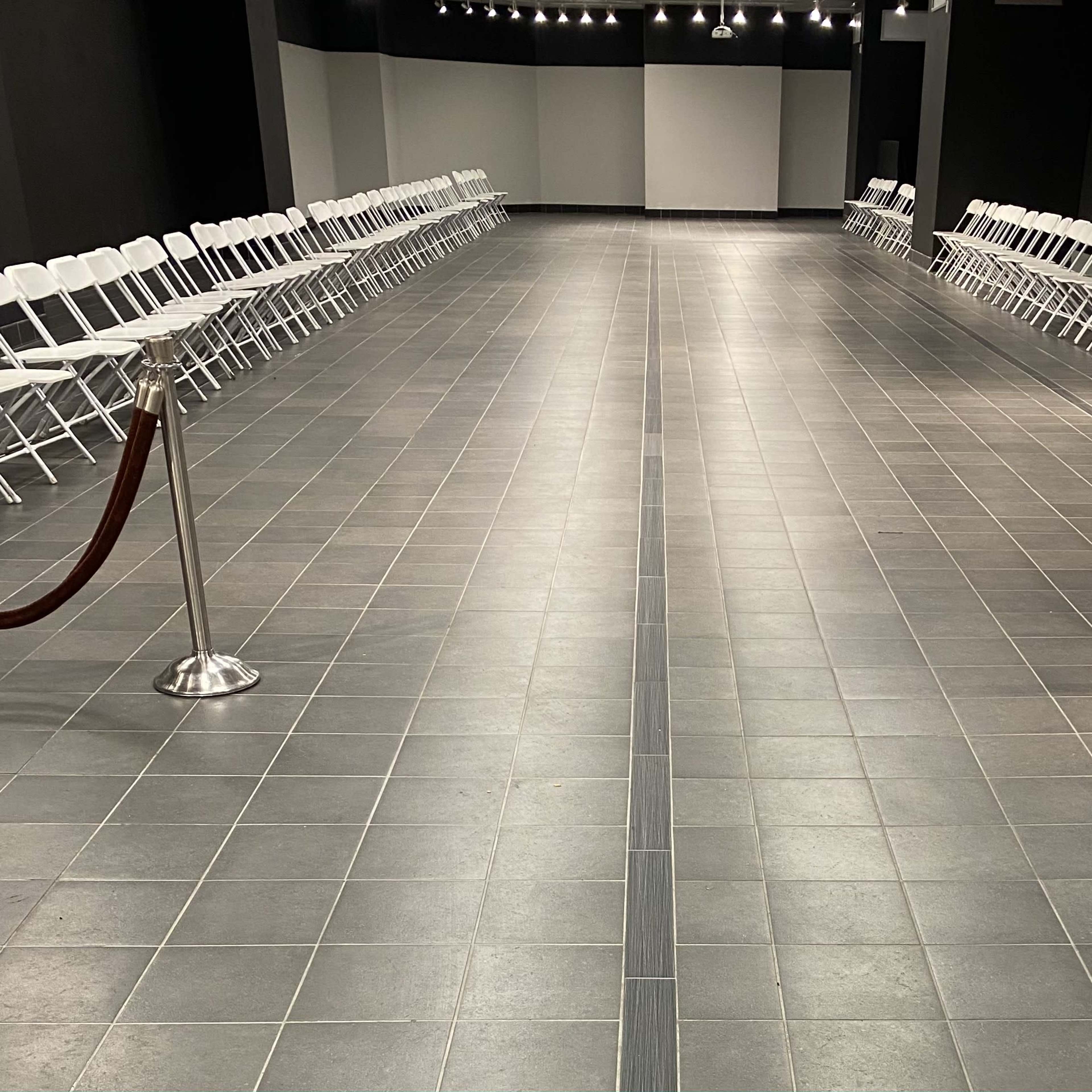 A spacious hall with two rows of white folding chairs arranged on either side of a central walkway, separated by a red rope barrier.