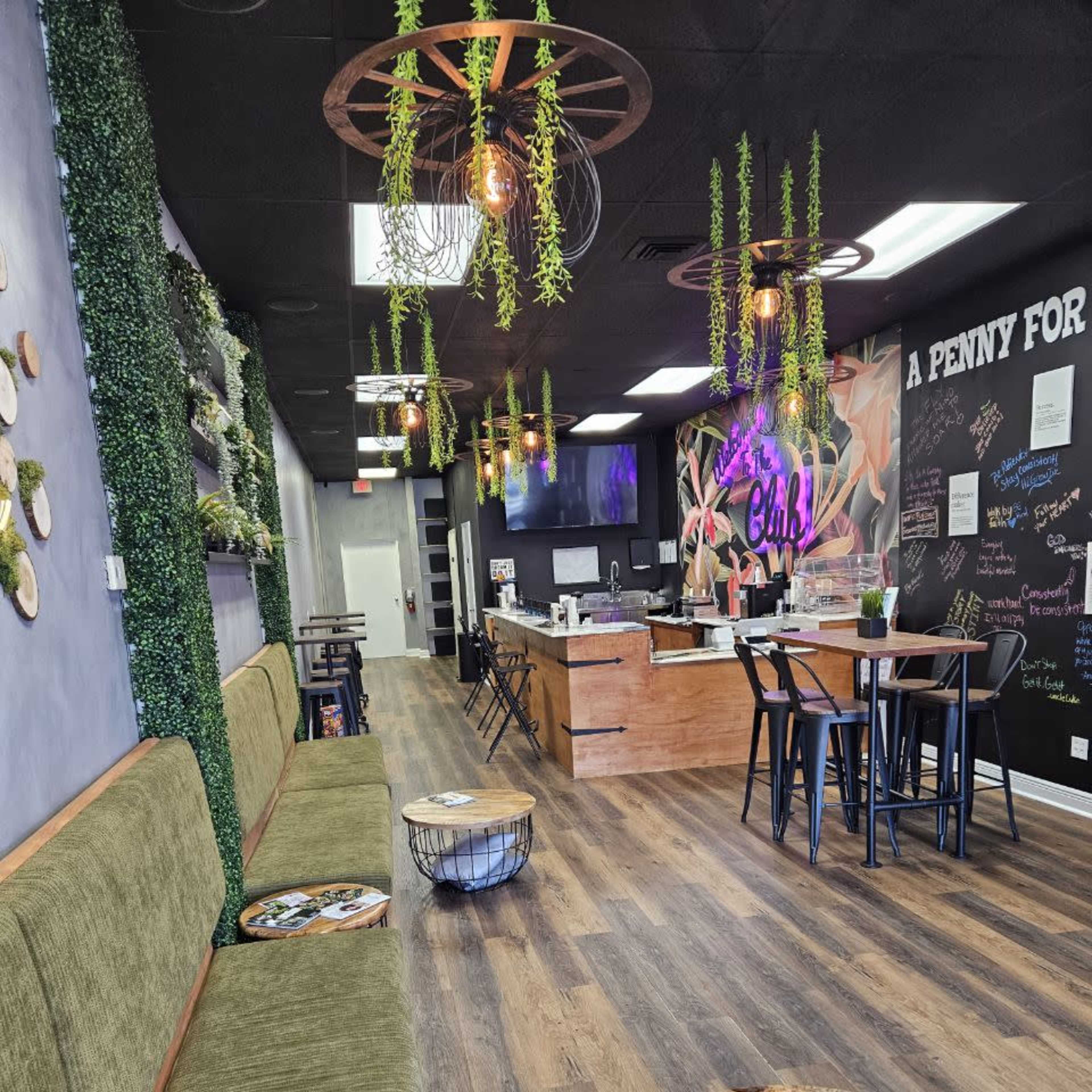 A modern interior of a café or lounge featuring green walls, wooden furniture, hanging plants, and stylized wall graphics.