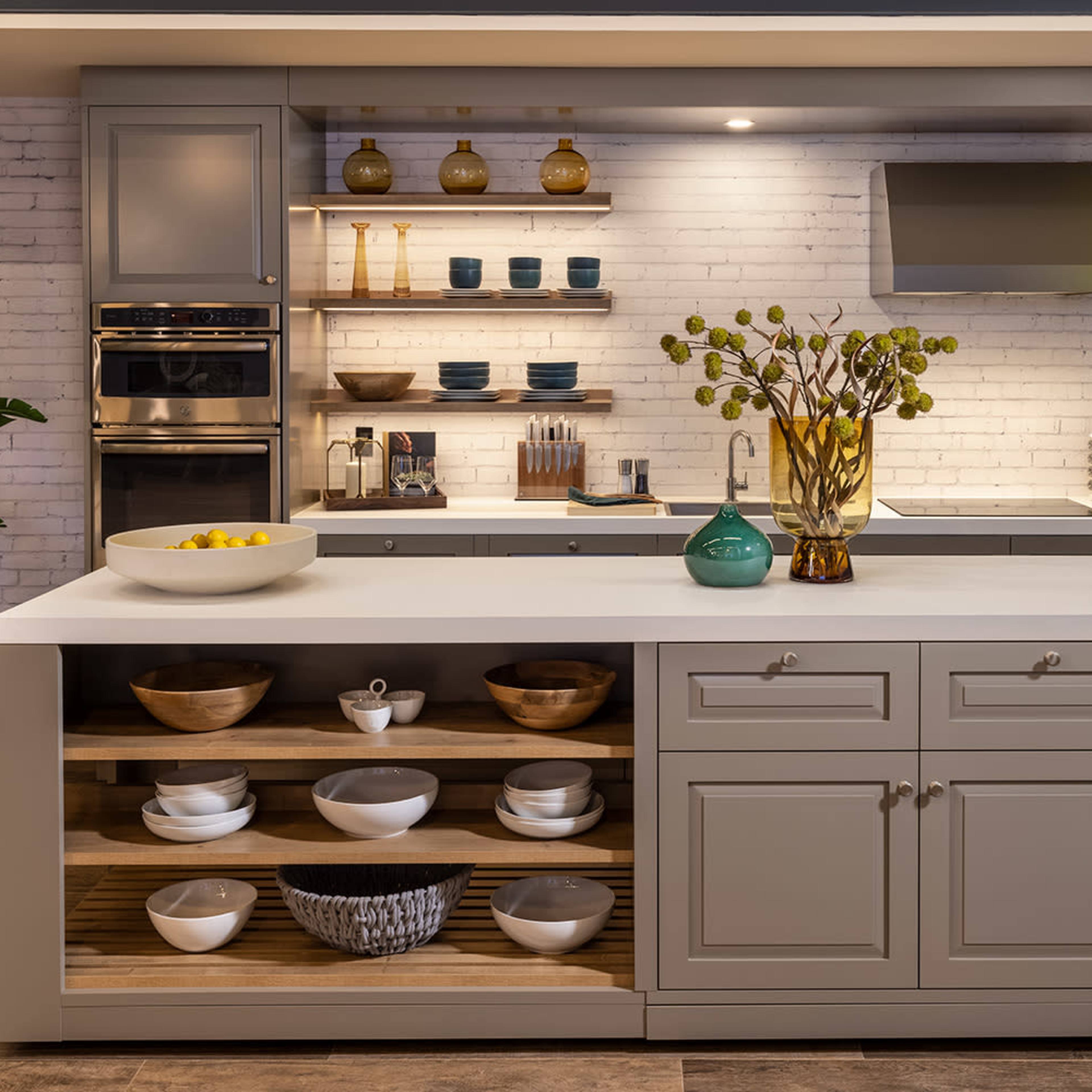 A modern kitchen features a central island with open shelving displaying various bowls and decorative items, complemented by a minimalist design and neutral cabinetry.