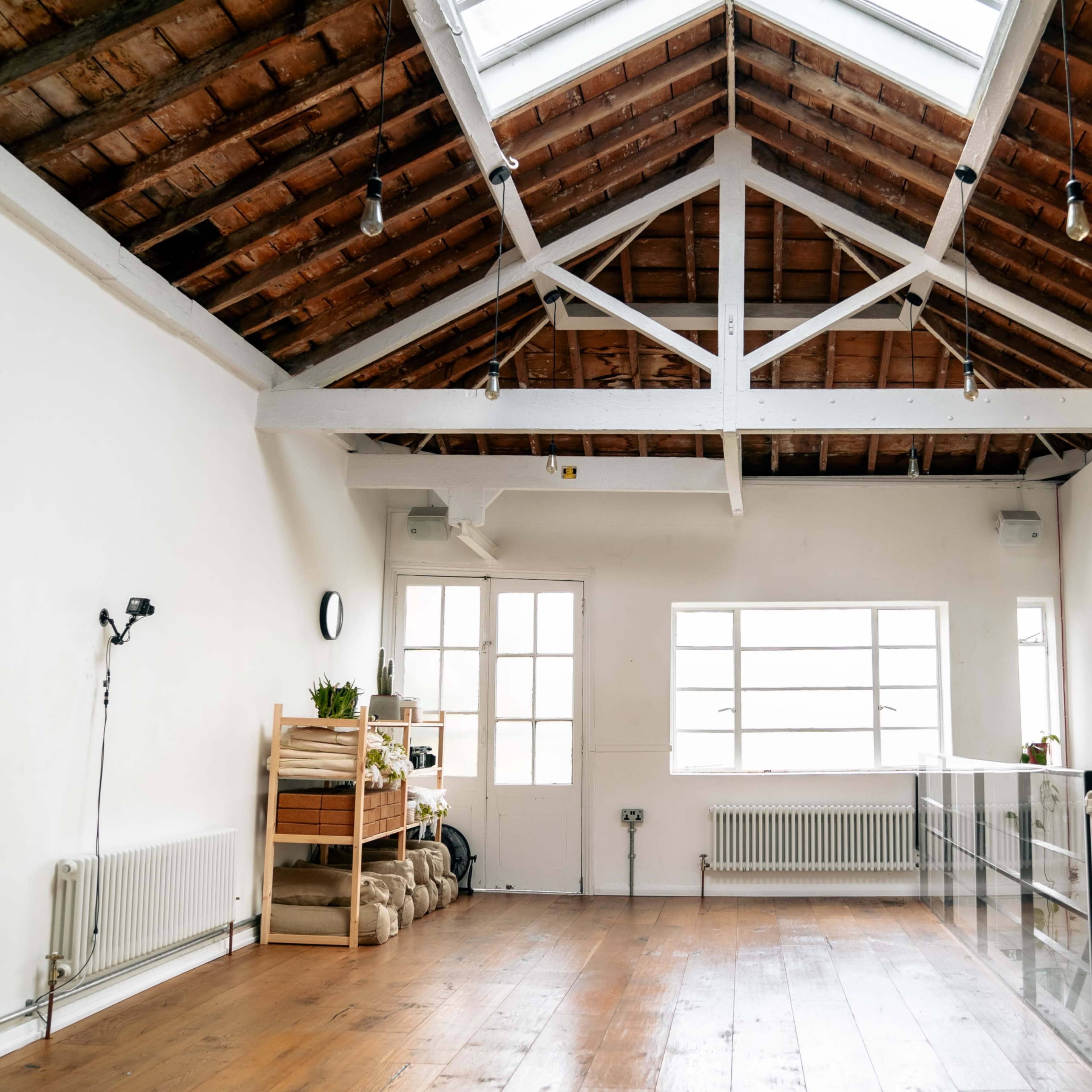 A spacious interior with a high, exposed beam ceiling, large windows, and wooden flooring, featuring minimal furnishings.