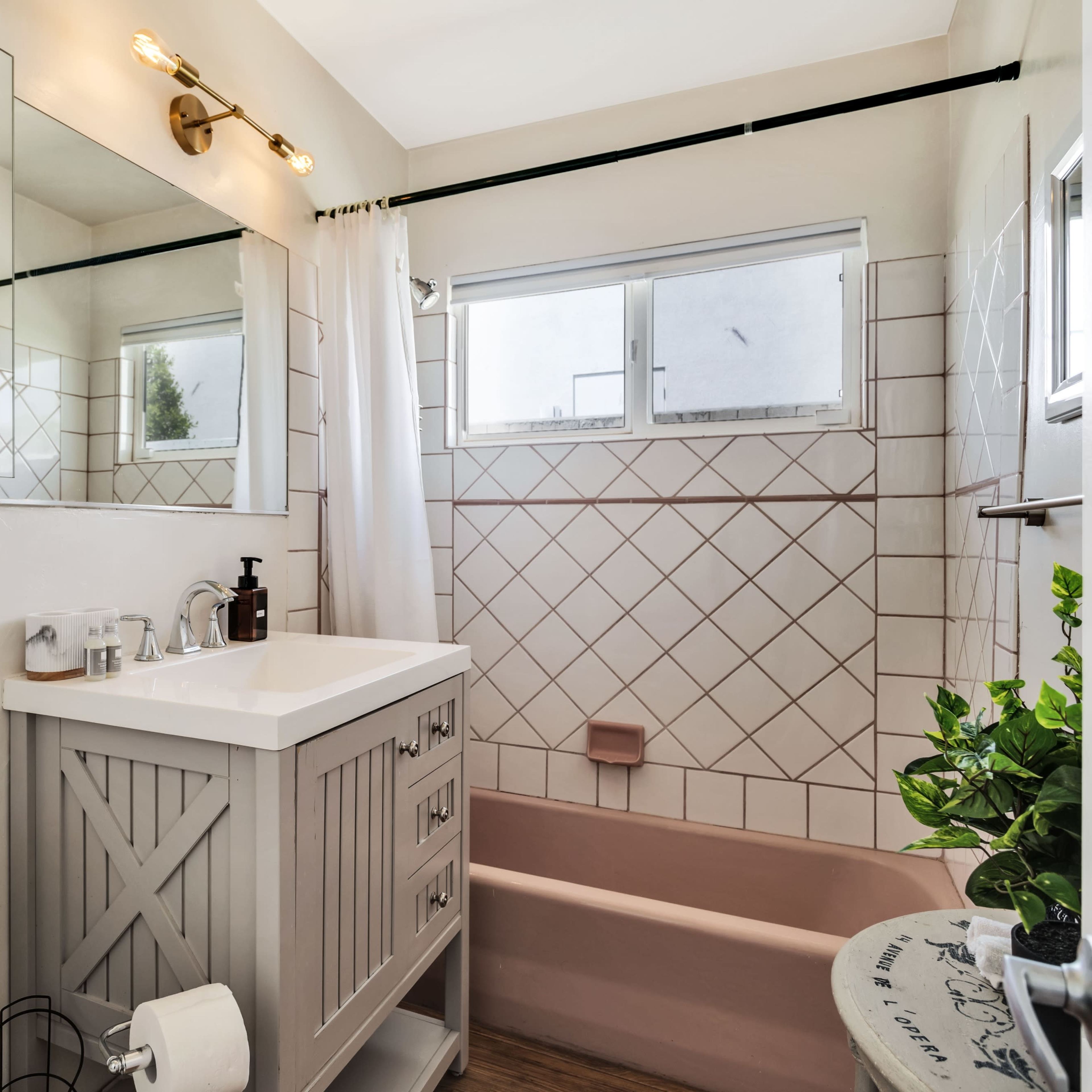A bathroom featuring a bathtub with a pink interior, a gray vanity with a basin, and tiled walls with a window allowing natural light.