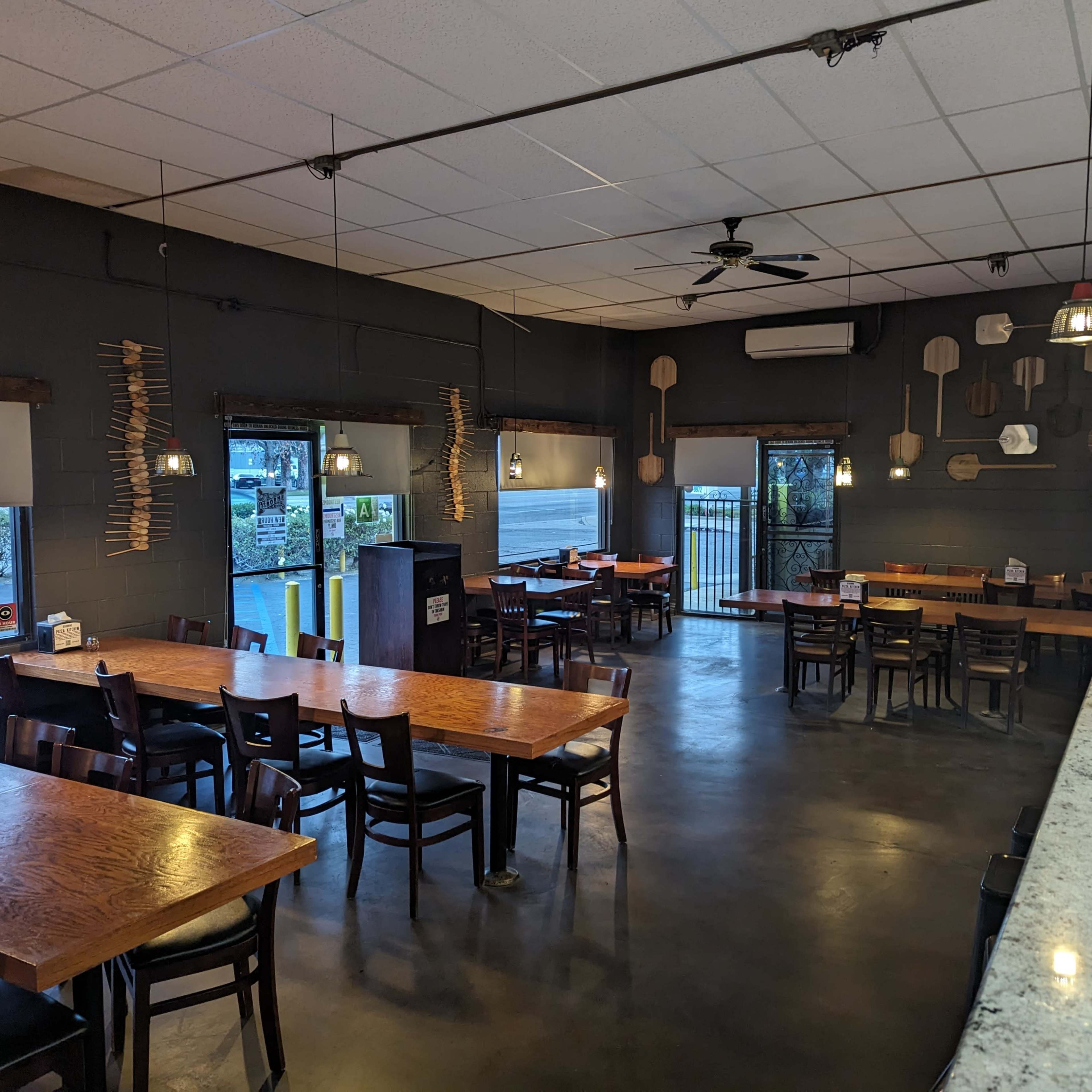 A spacious restaurant interior with wooden tables and chairs, pendant lighting, and a granite countertop, featuring a chef figurine on the counter.