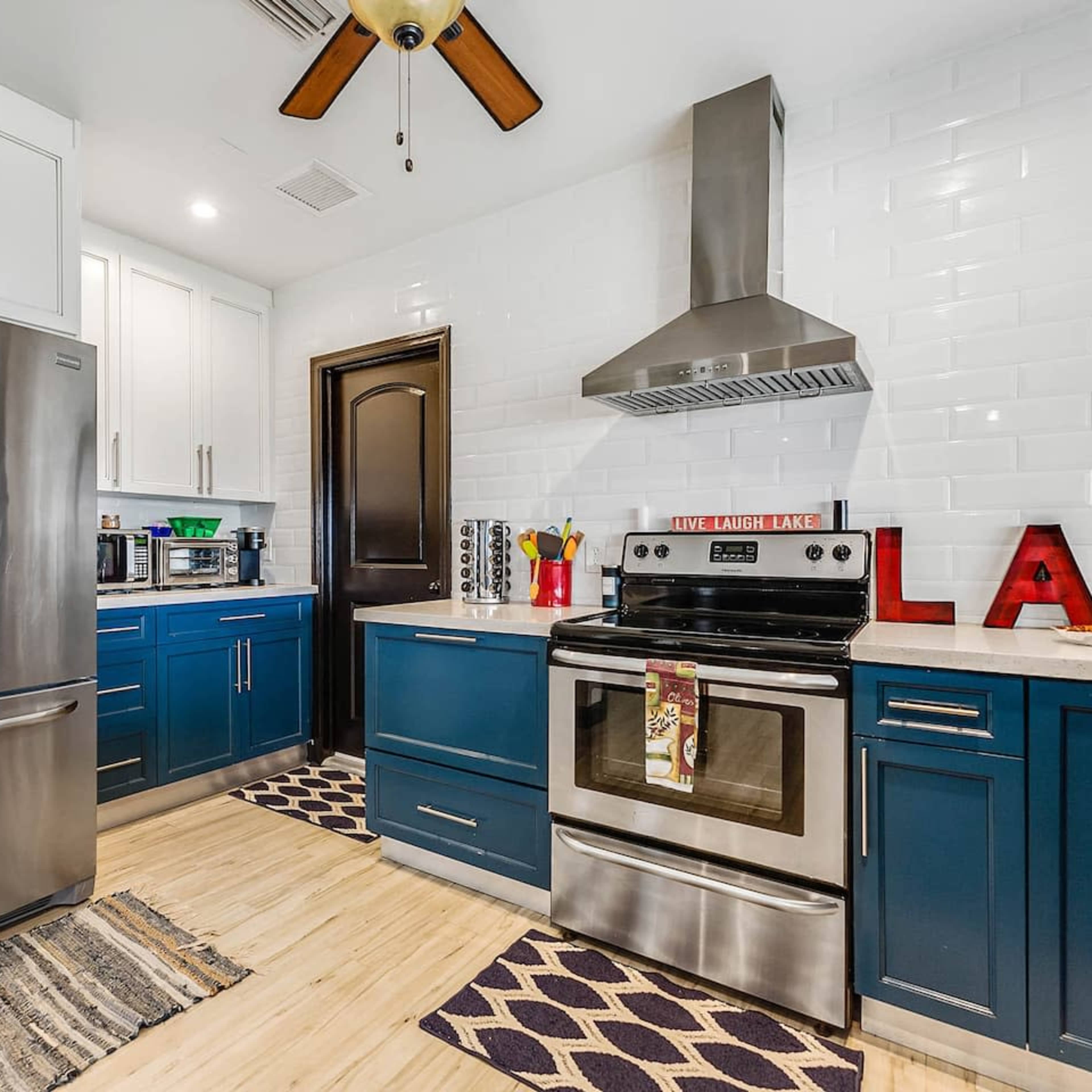 A modern kitchen features stainless steel appliances, blue cabinets, and a decorative sign spelling "LAKE."