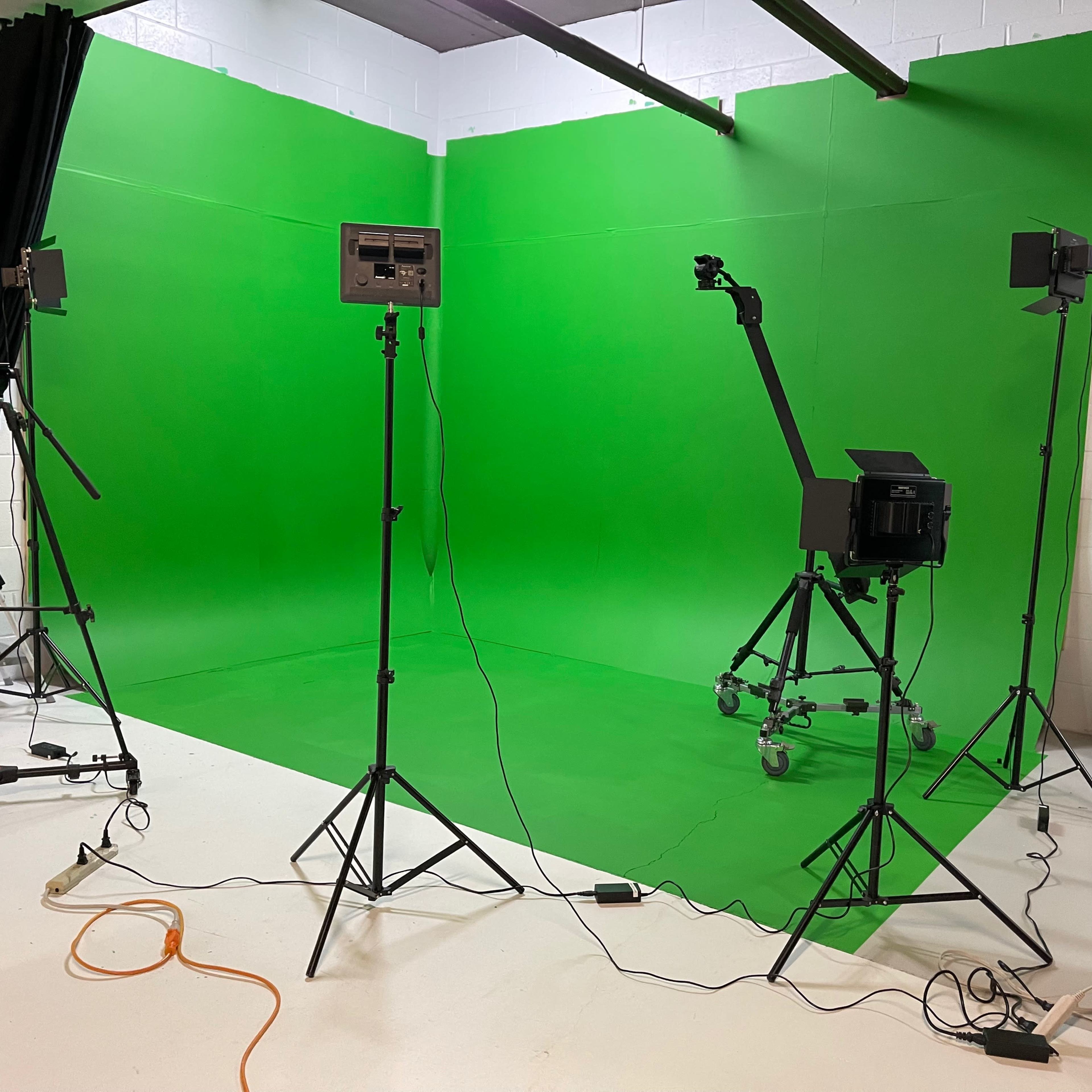 A studio setup with a green screen background, multiple lighting stands, and various equipment arranged on a white floor.