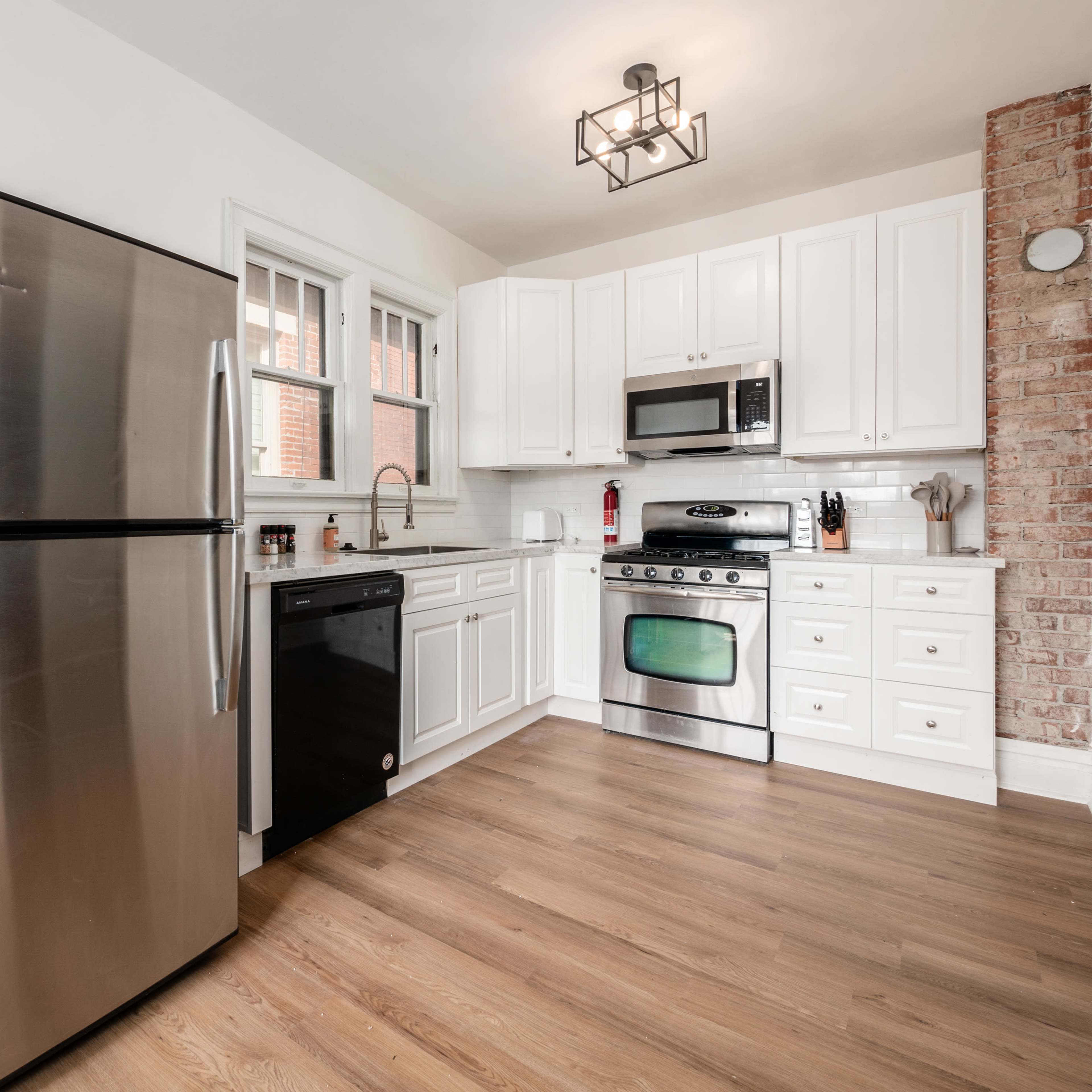 A modern kitchen features stainless steel appliances, white cabinetry, and a brick accent wall.