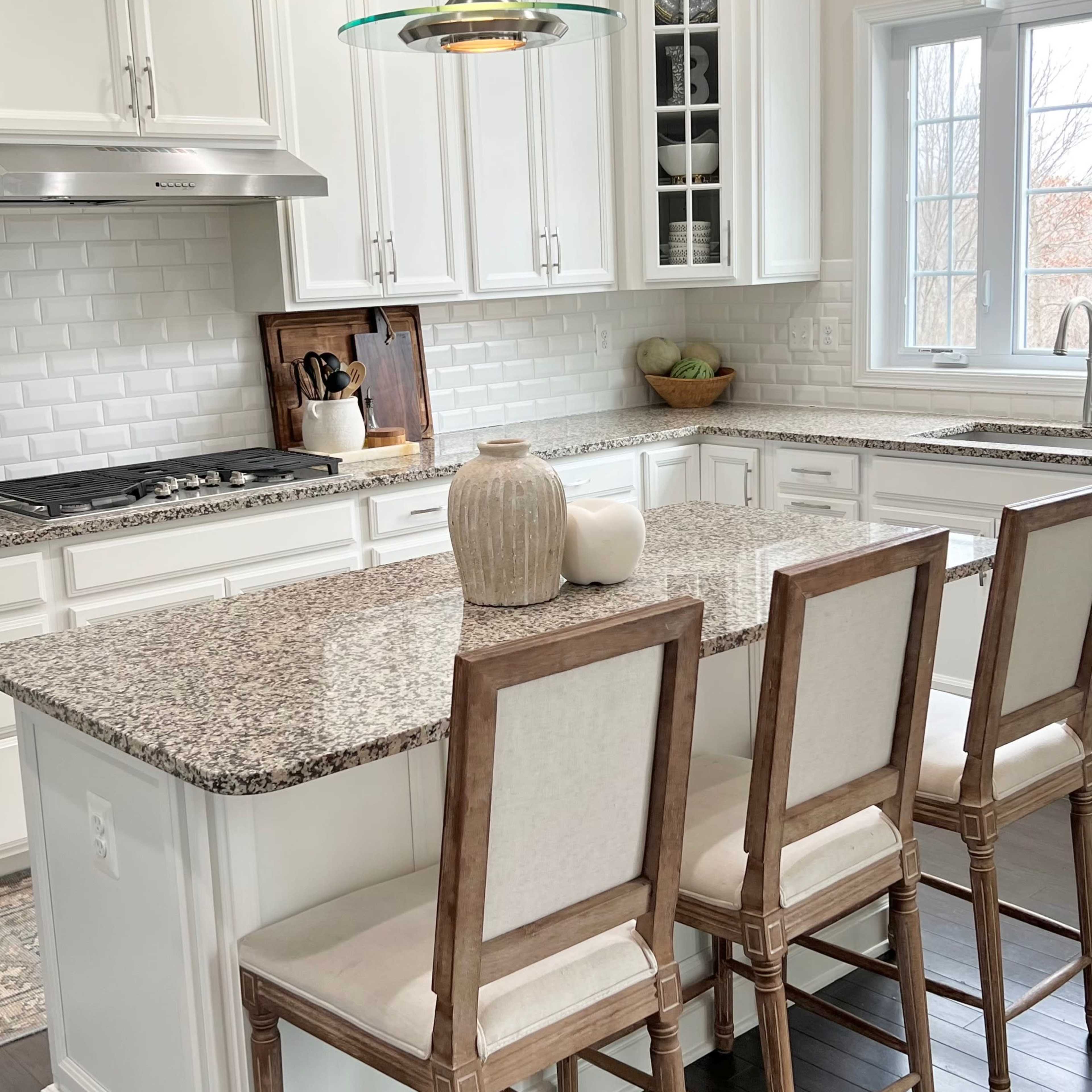 A modern kitchen features white cabinetry, a large granite island with seating, and a pendant light above.
