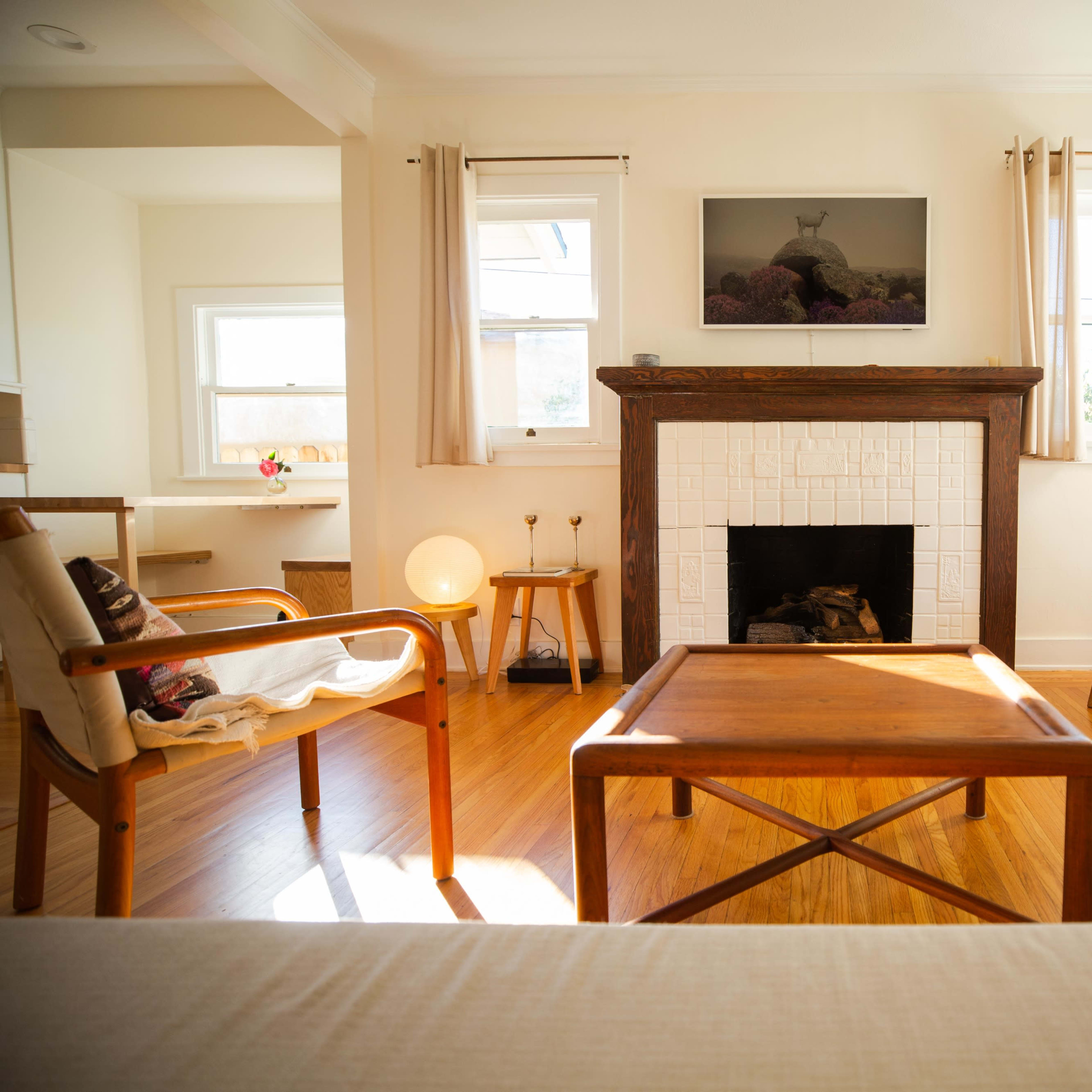 The room features a wooden coffee table at the center, surrounded by chairs and a fireplace, with large windows allowing natural light to fill the space.