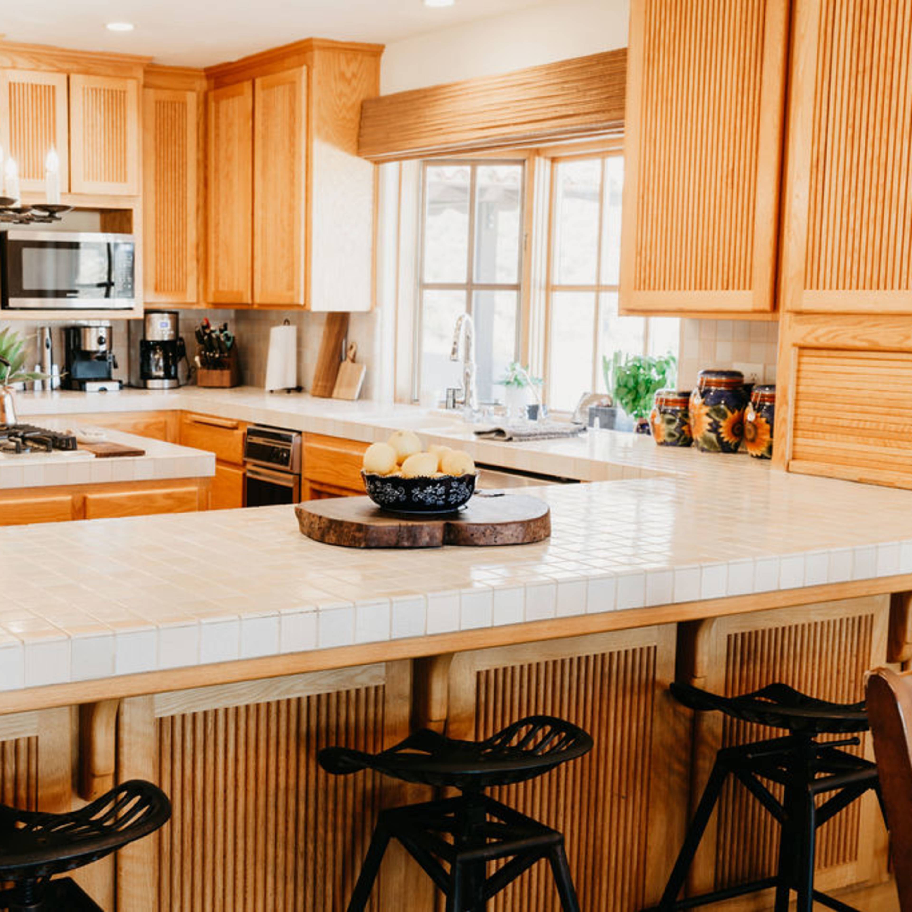 A large, open kitchen features wooden cabinetry, a tiled island with seating, and a window that lets in natural light.