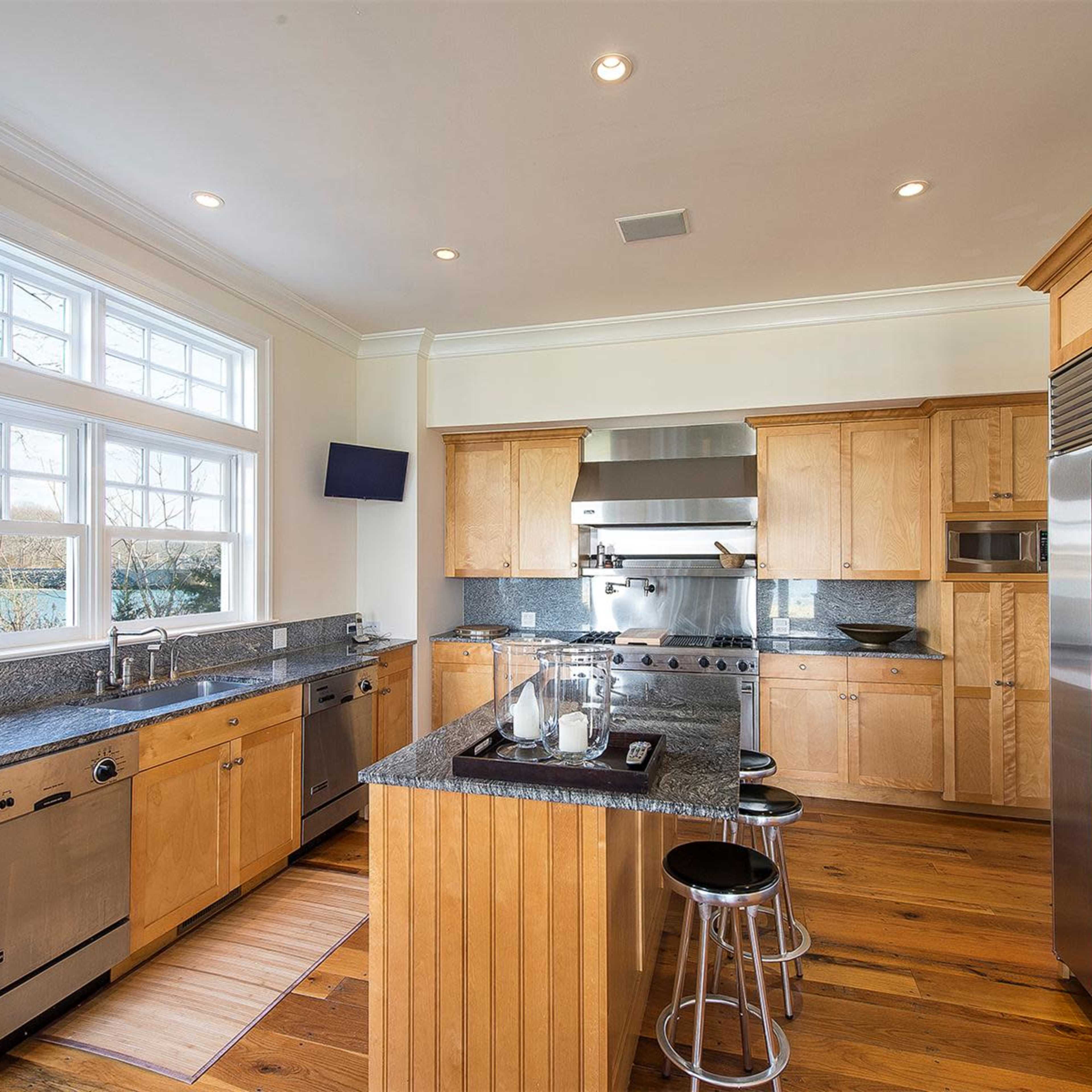 The kitchen features wooden cabinets, granite countertops, stainless steel appliances, and large windows allowing natural light.