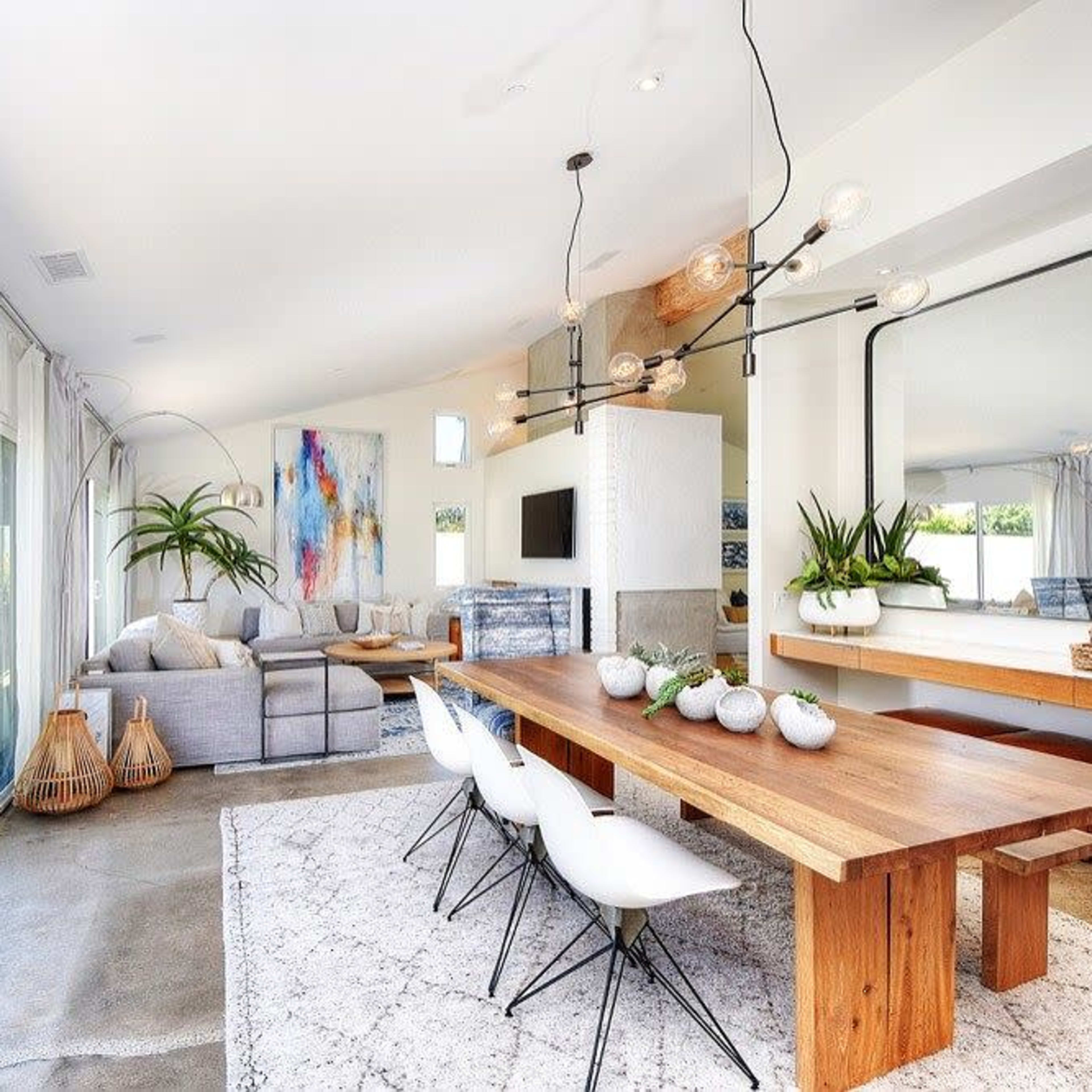 A modern living space featuring a wooden dining table, white chairs, a gray sofa, and large windows letting in natural light.
