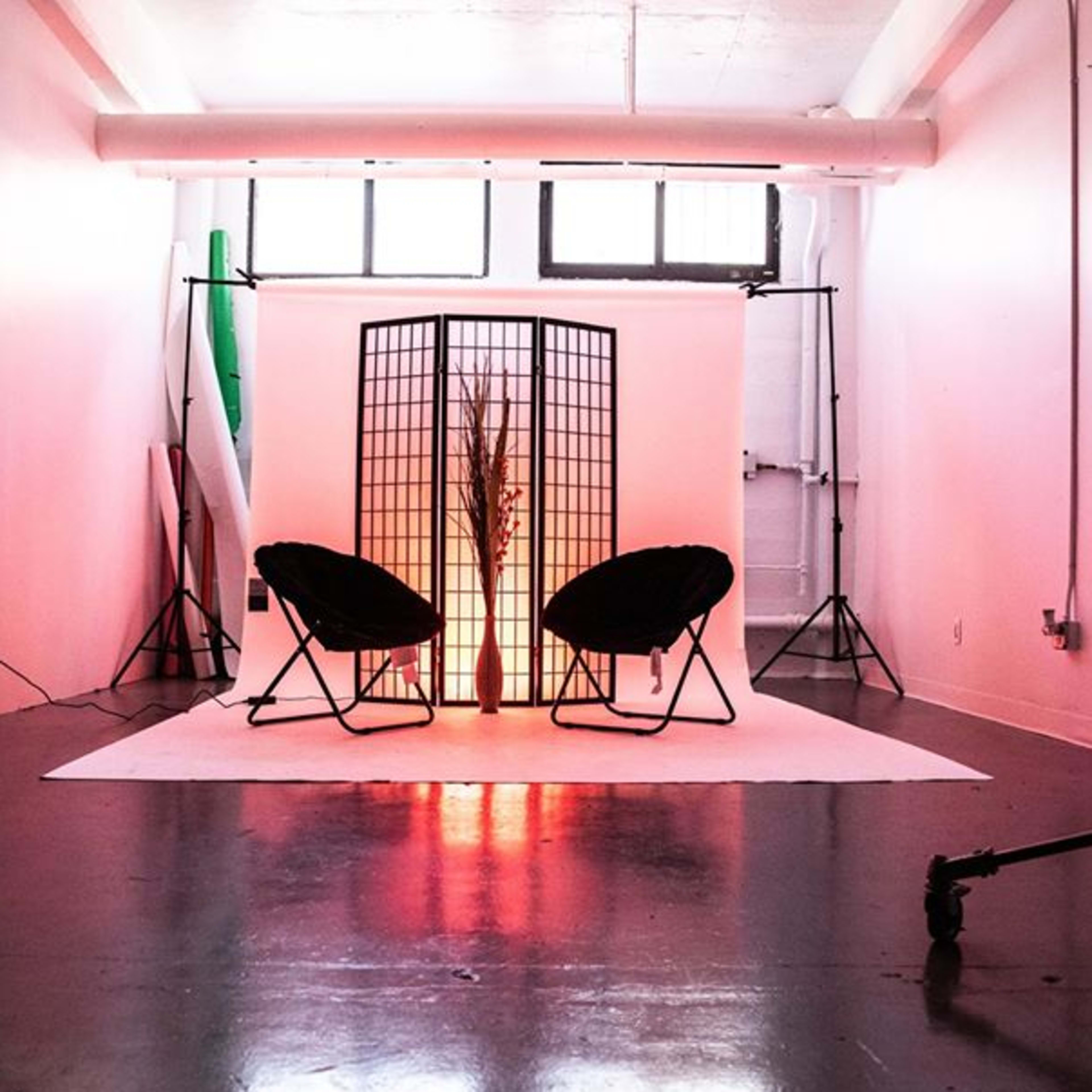 A studio setup featuring two chairs facing a decorative screen, illuminated by soft light, with a backdrop of various photography equipment and colored backgrounds.