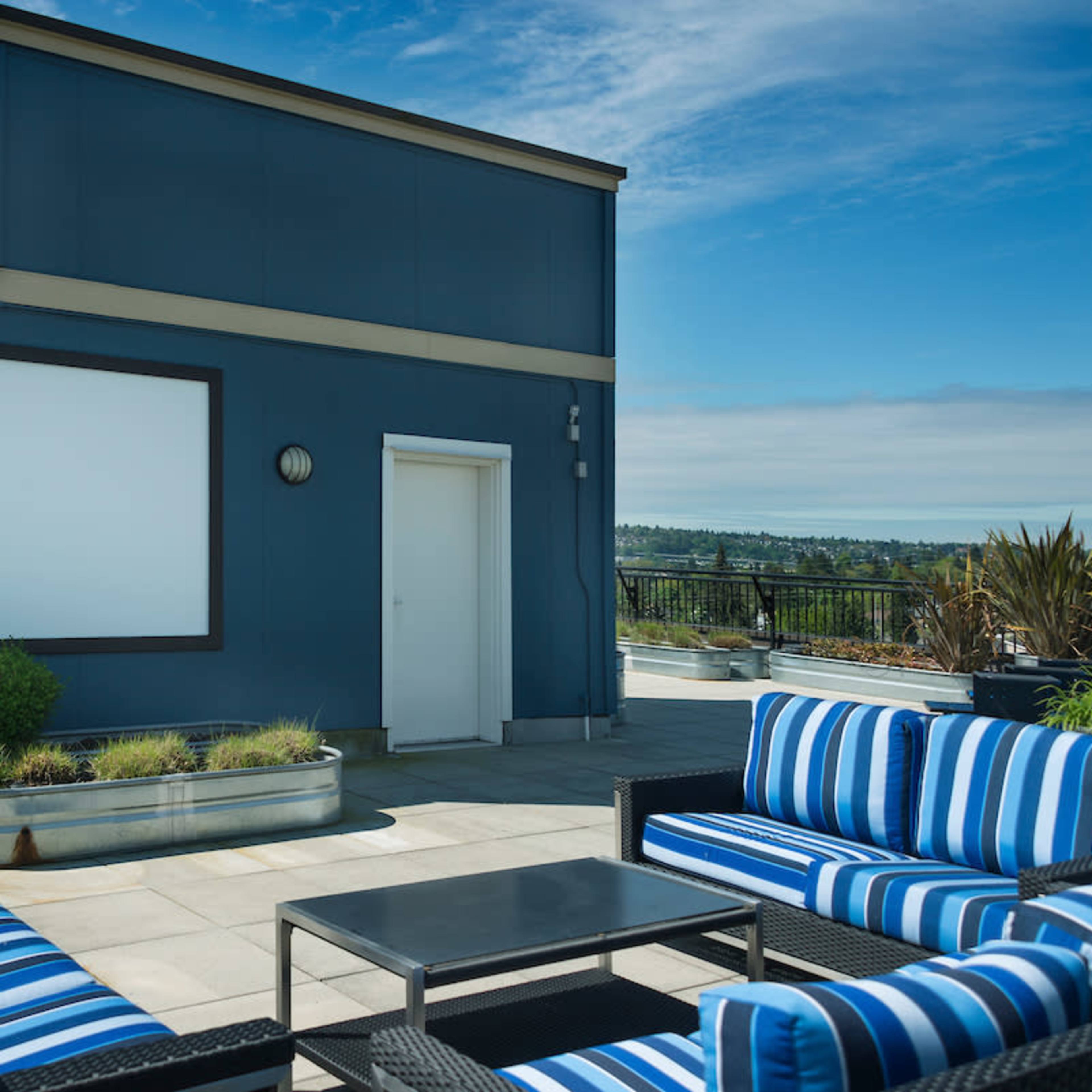 A rooftop patio features striped seating, a coffee table, and a blank screen mounted on the wall.