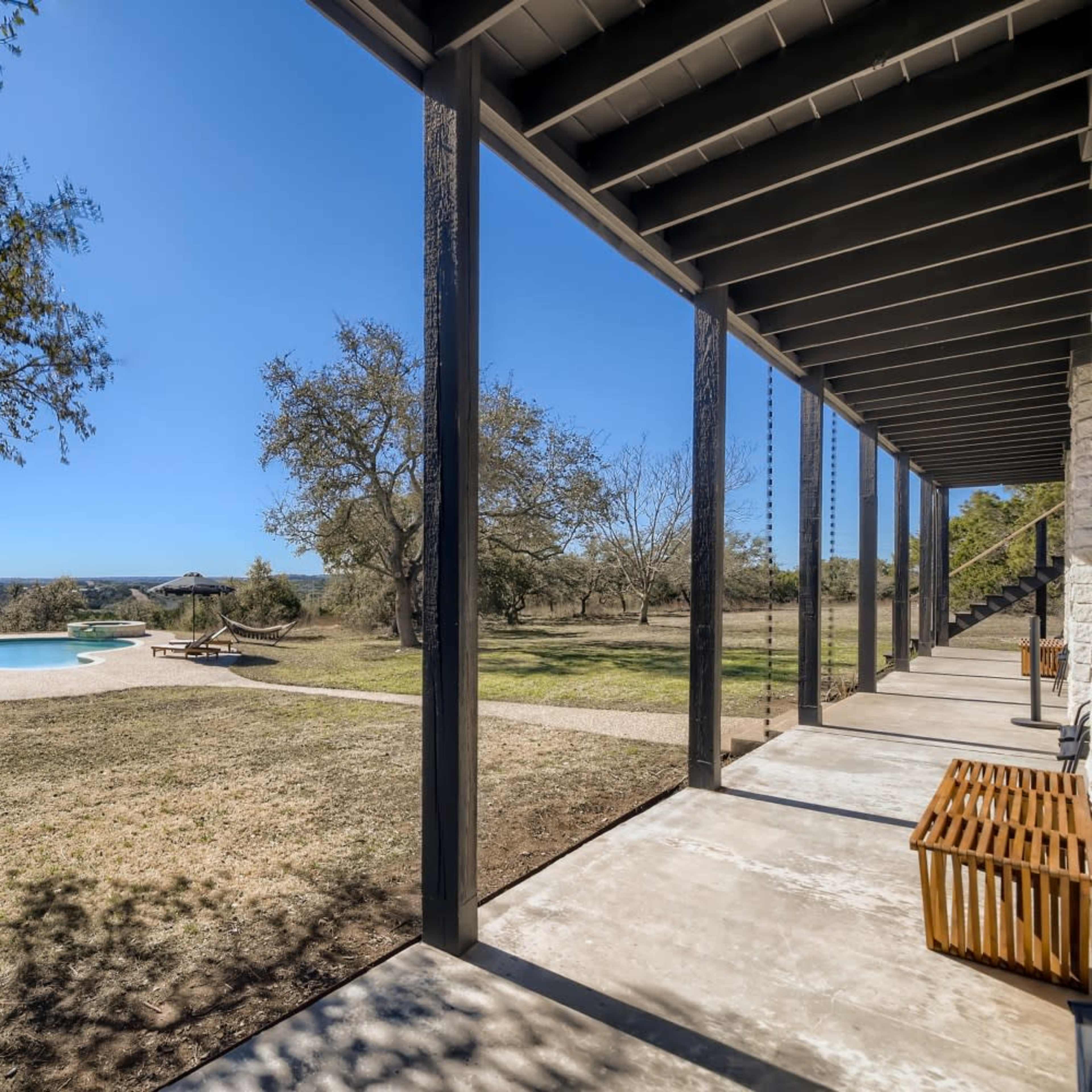 A scenic outdoor area with a pool, sun loungers, and a covered porch extending towards the horizon.