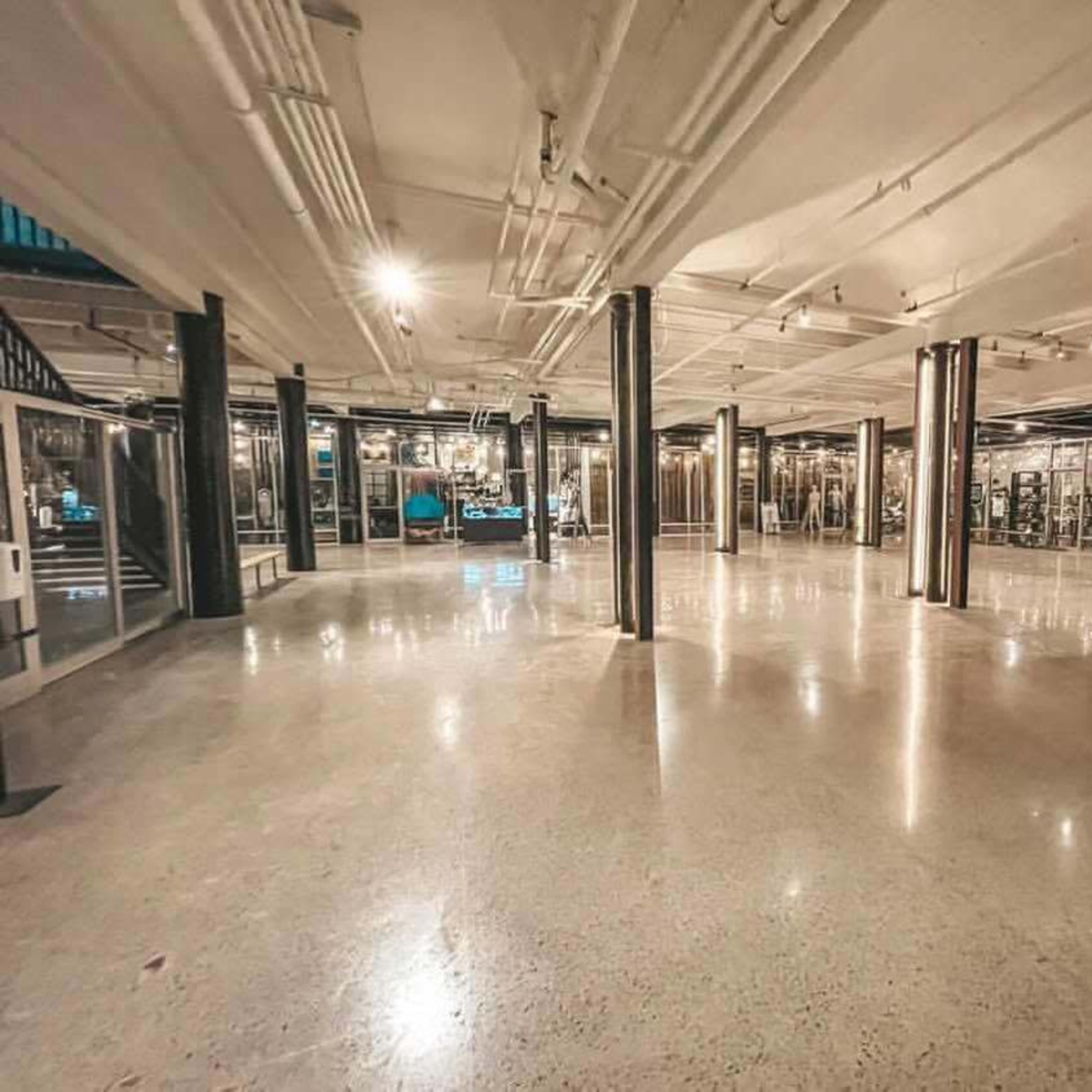 A spacious, empty industrial-style interior with polished concrete floors and exposed pipes.