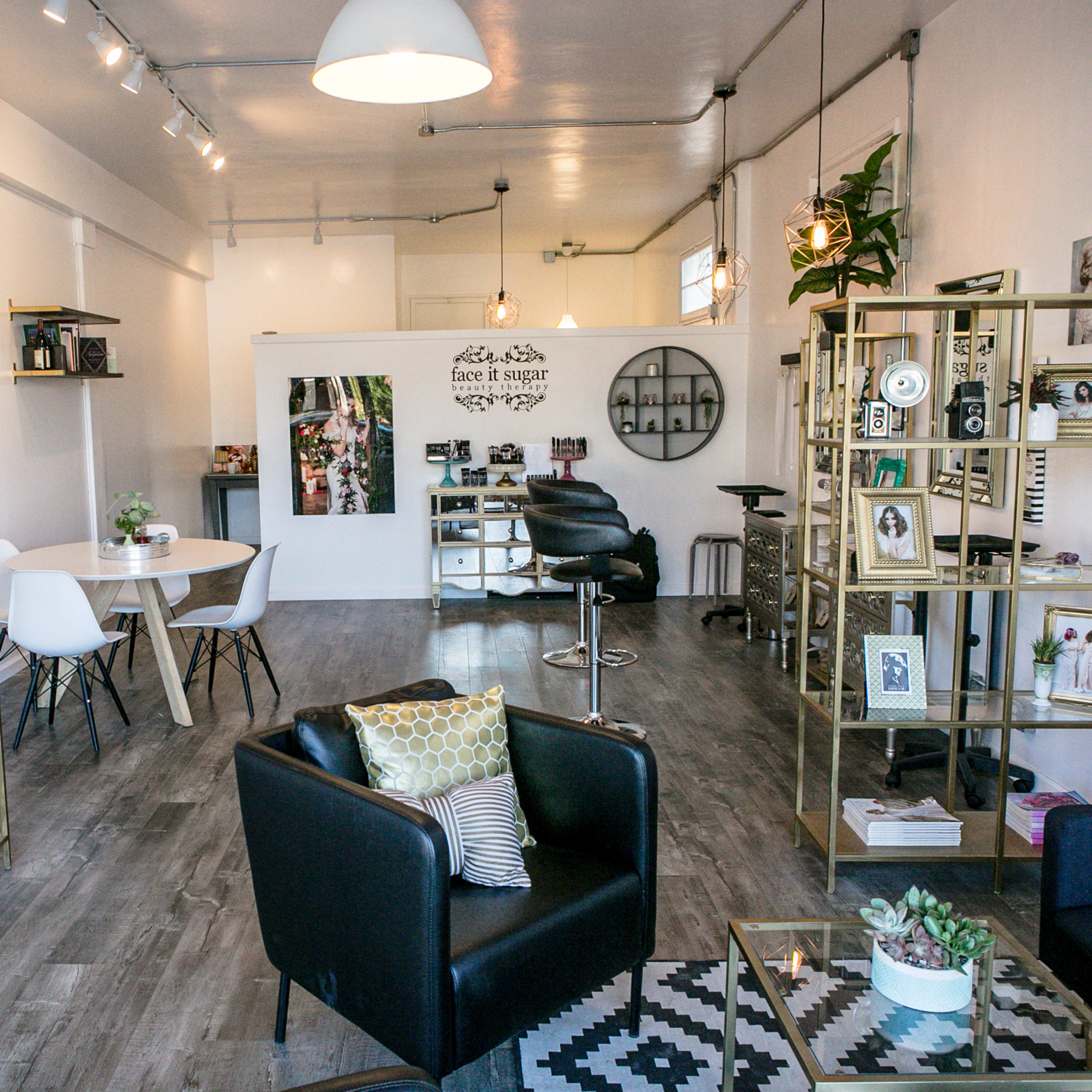 A modern interior space featuring wooden flooring, sleek furniture, gold shelving units, and a mix of decorative items and plants.