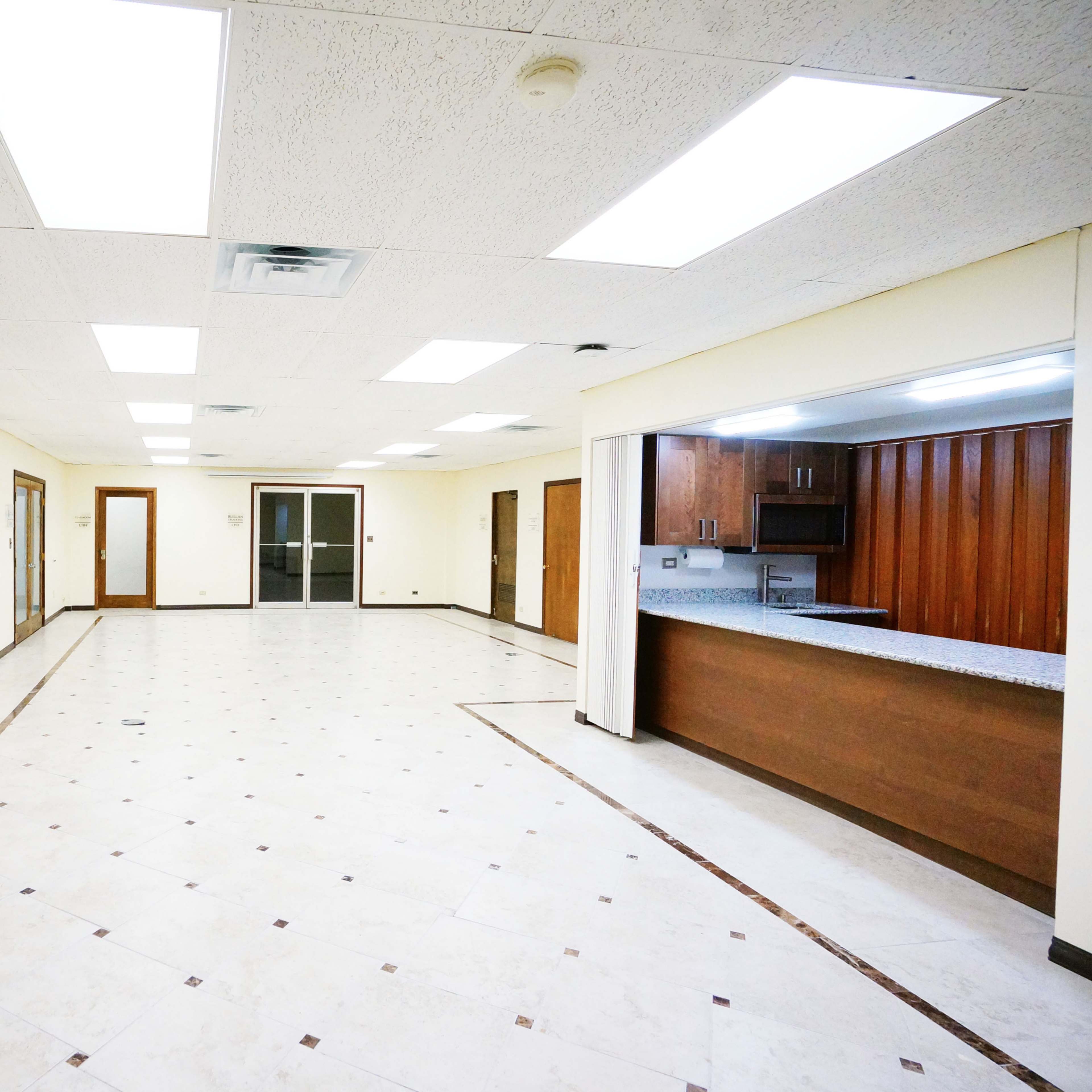 A spacious, empty room with tiled flooring, a large wall mural of a pathway, and an open kitchen area in the background.