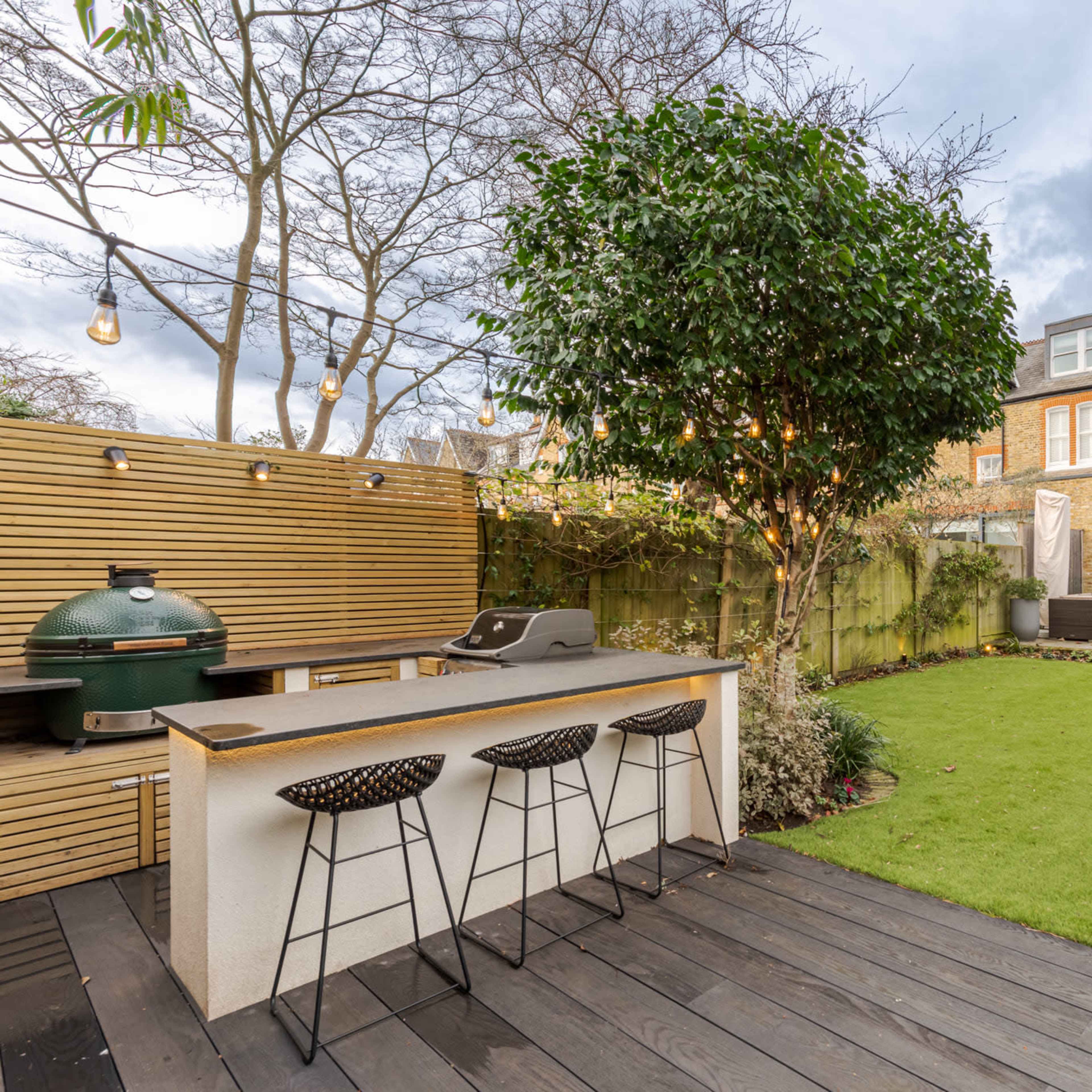 A landscaped backyard featuring a green lawn, a modern outdoor kitchen with seating, and a contemporary home in the background.