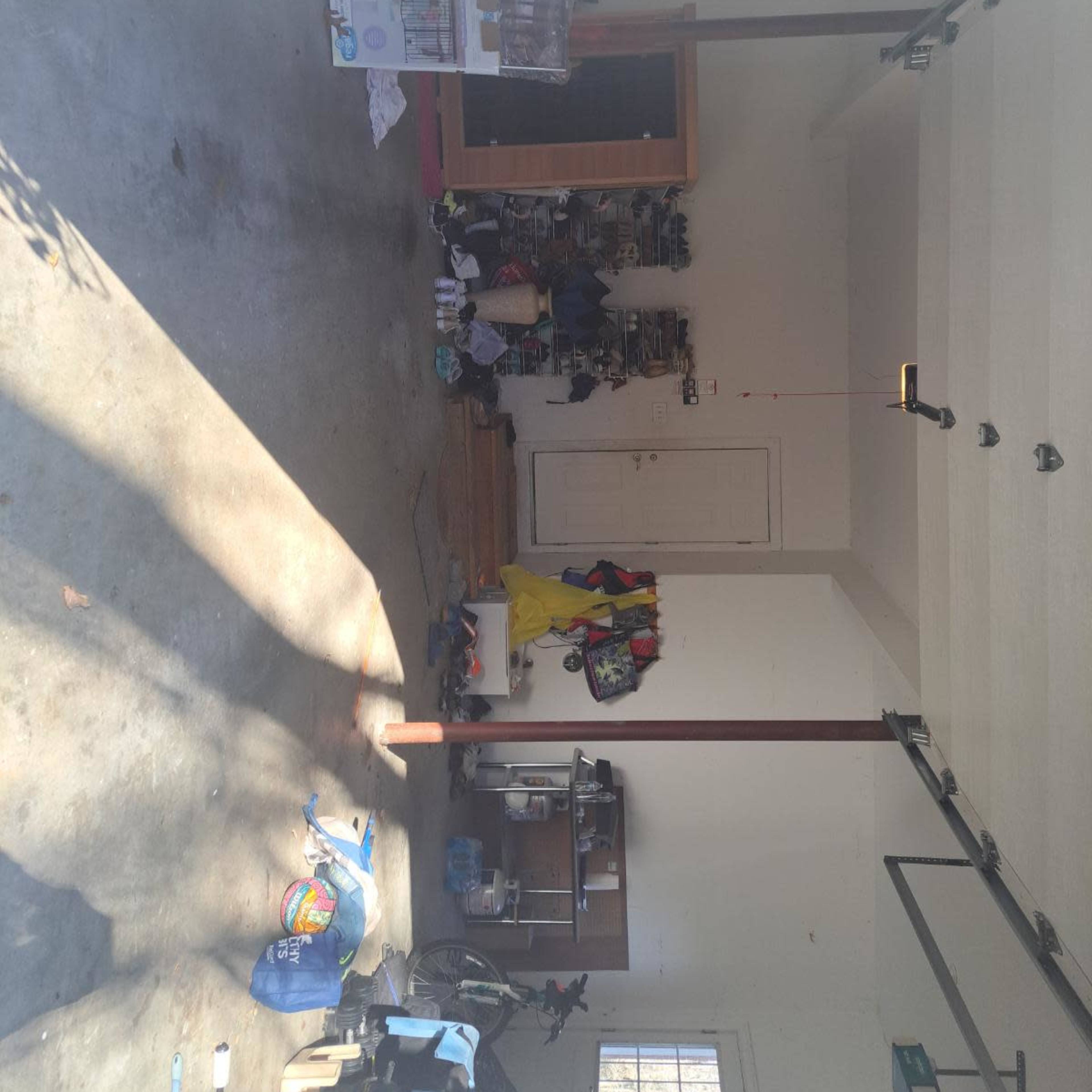 A cluttered garage with various items scattered on the floor and shelves against the walls.