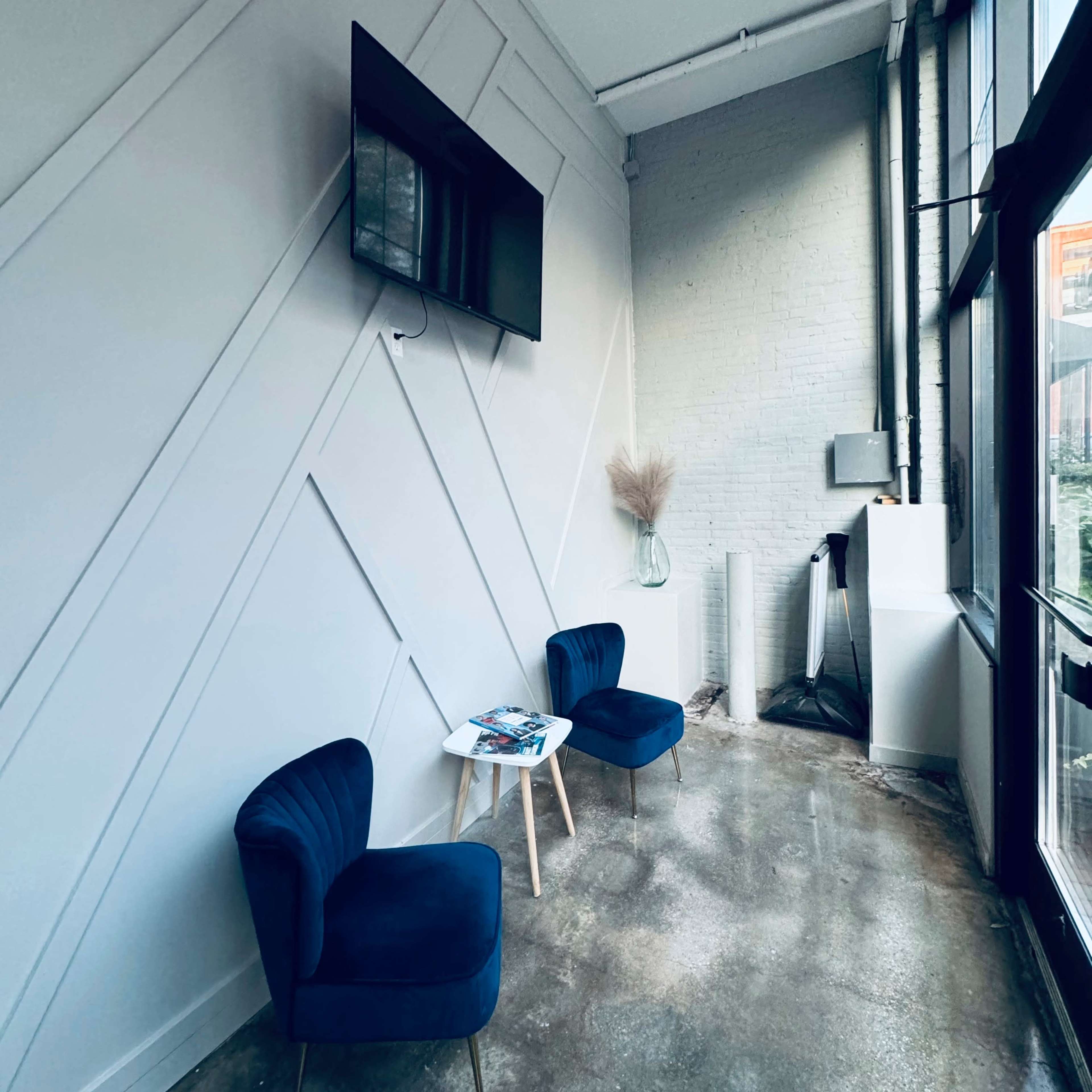 A minimalist corner with two blue chairs, a small coffee table, and a wall-mounted television in an industrial-style room.