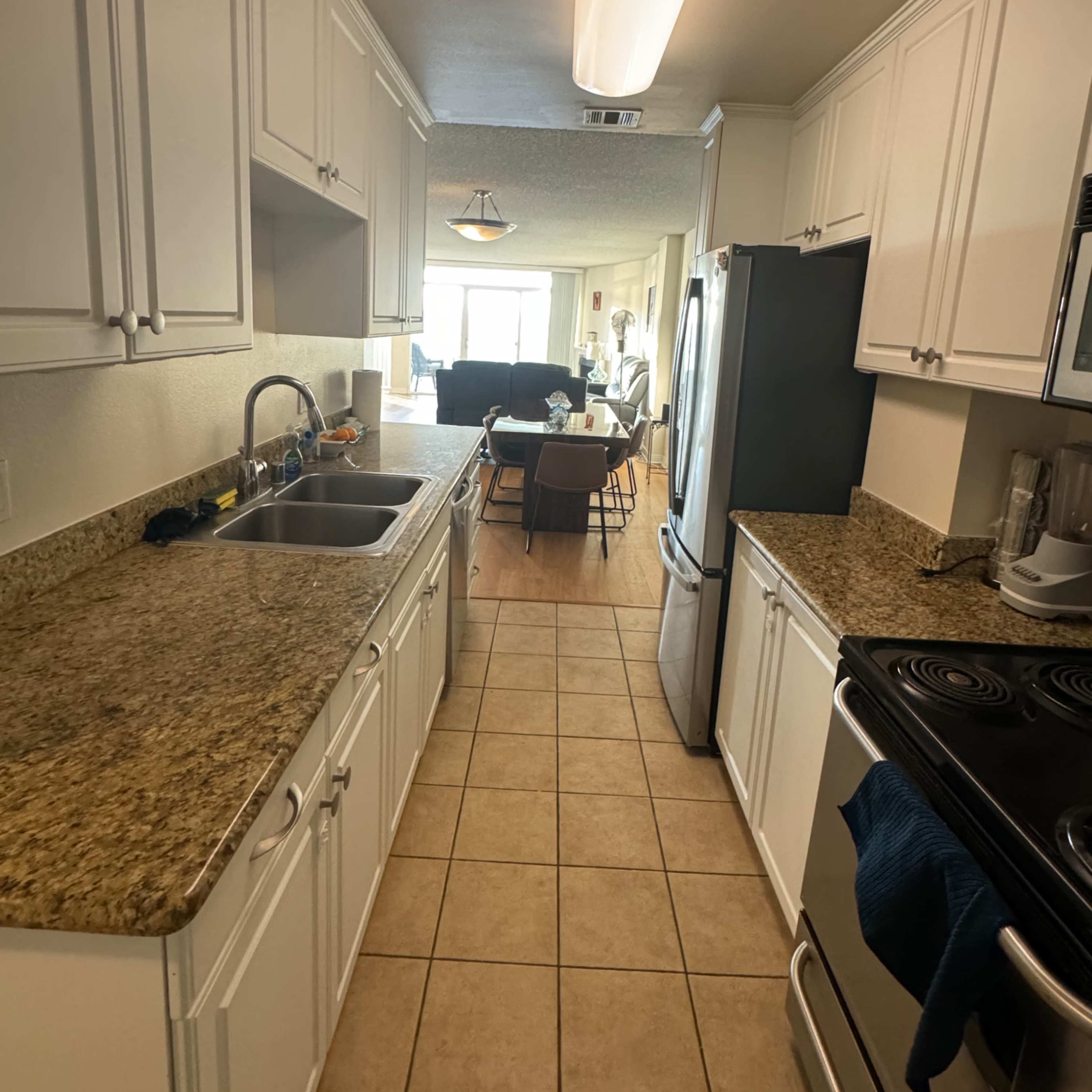 A galley kitchen with white cabinets, granite countertops, and a view into a dining area featuring a table and chairs.