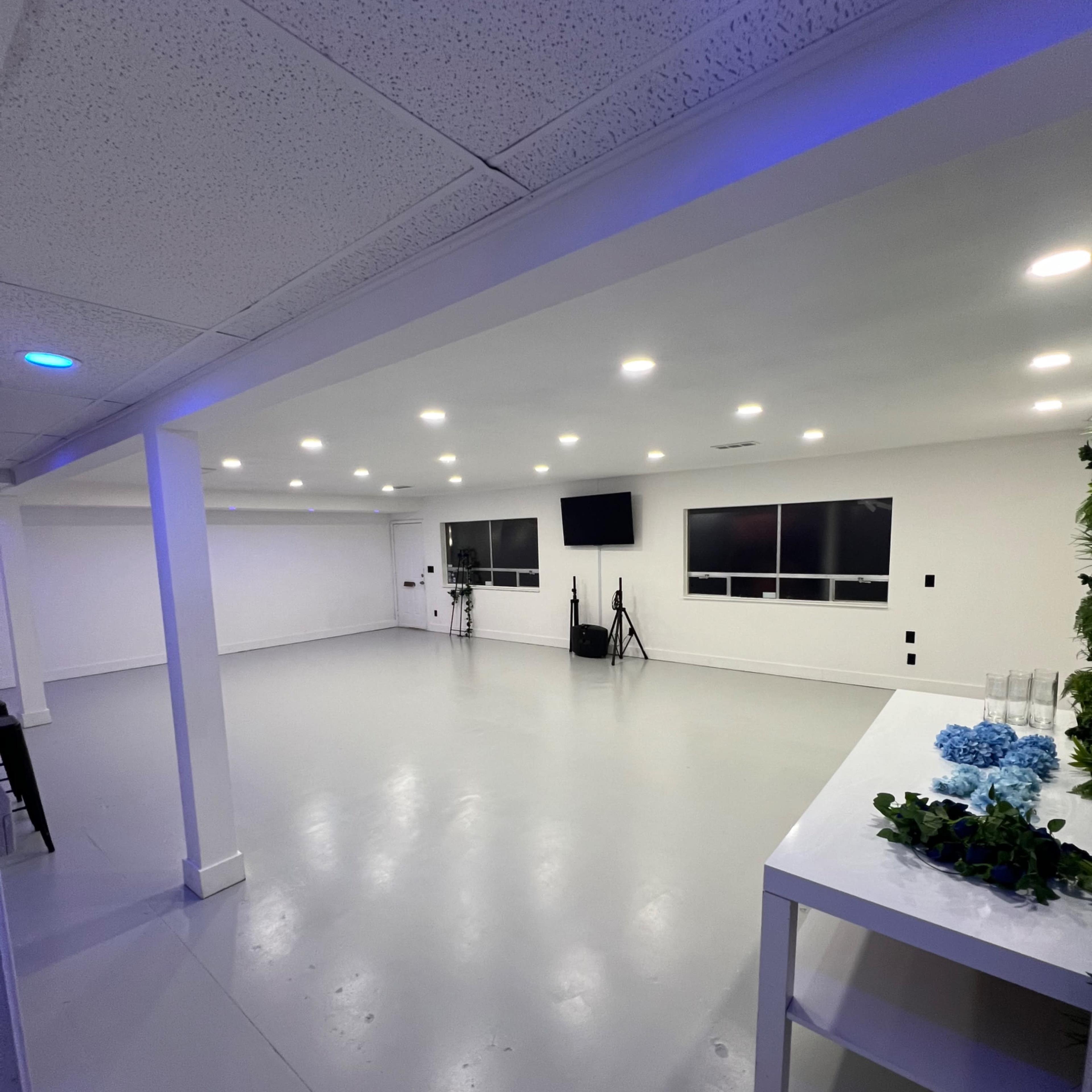 A spacious, well-lit room with gray flooring, white walls, and two televisions mounted on the walls.