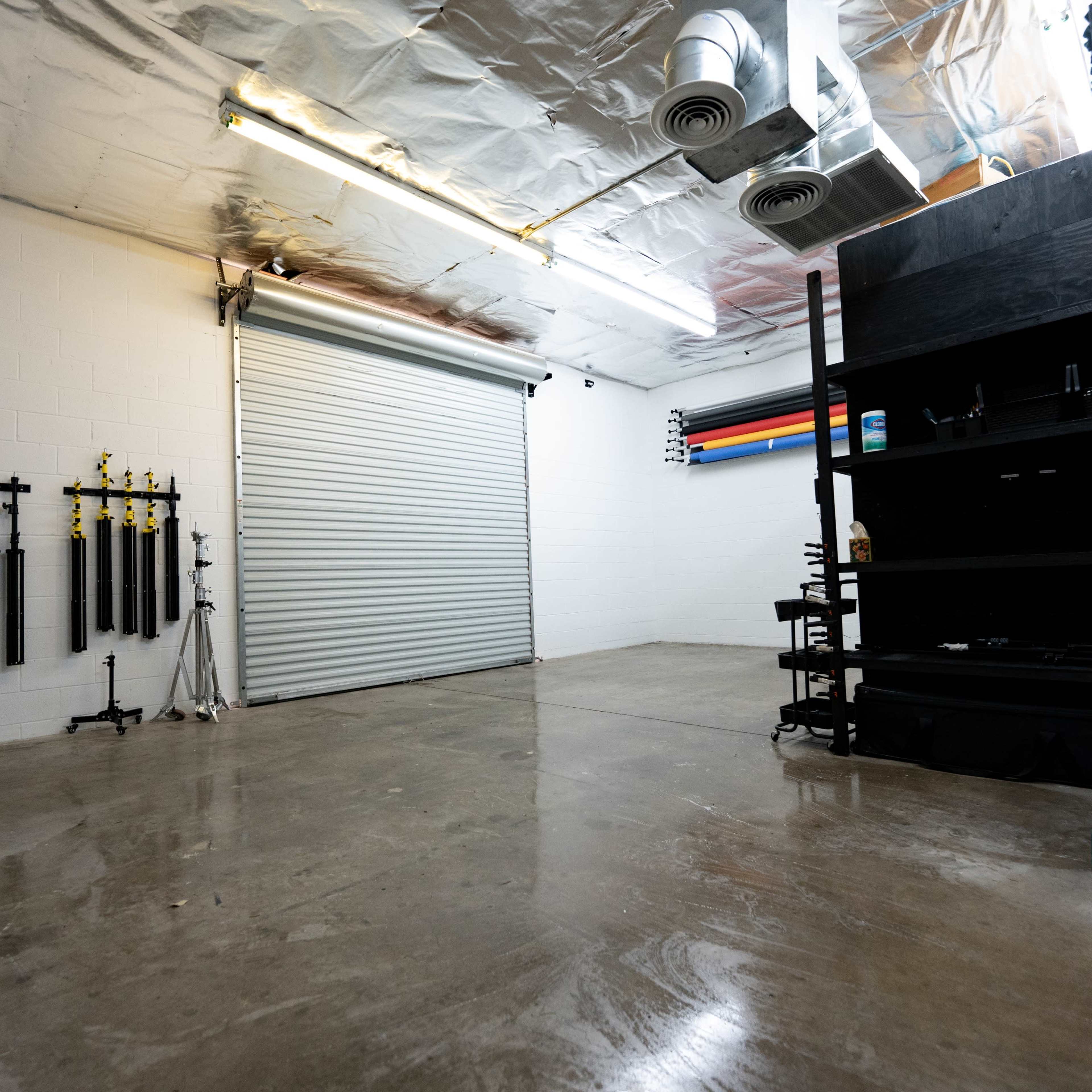 A spacious, clean garage or workshop with a sectional roll-up door, concrete floor, and equipment storage on one side.