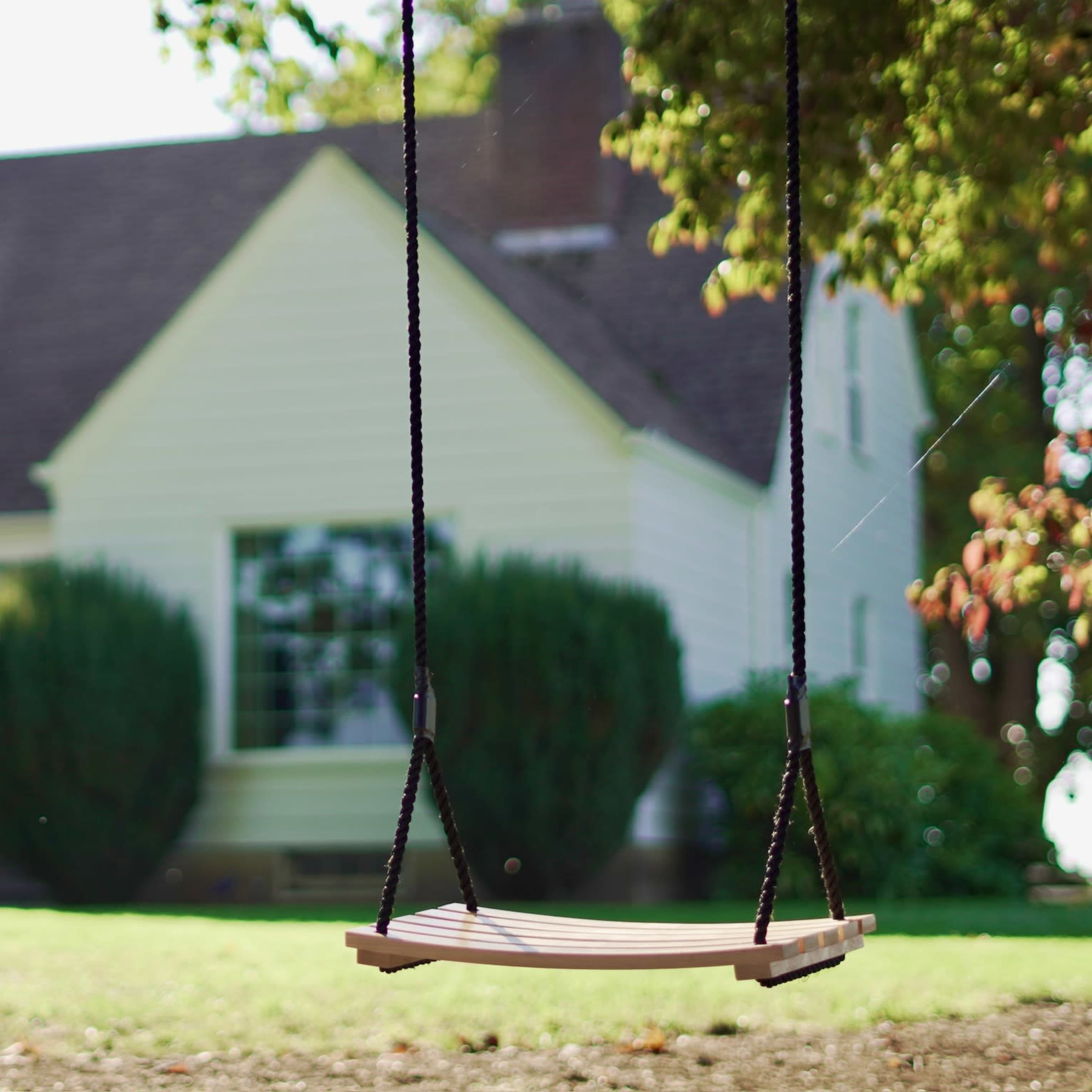 A wooden swing hangs from a rope in the foreground, with a house and garden visible in the background.