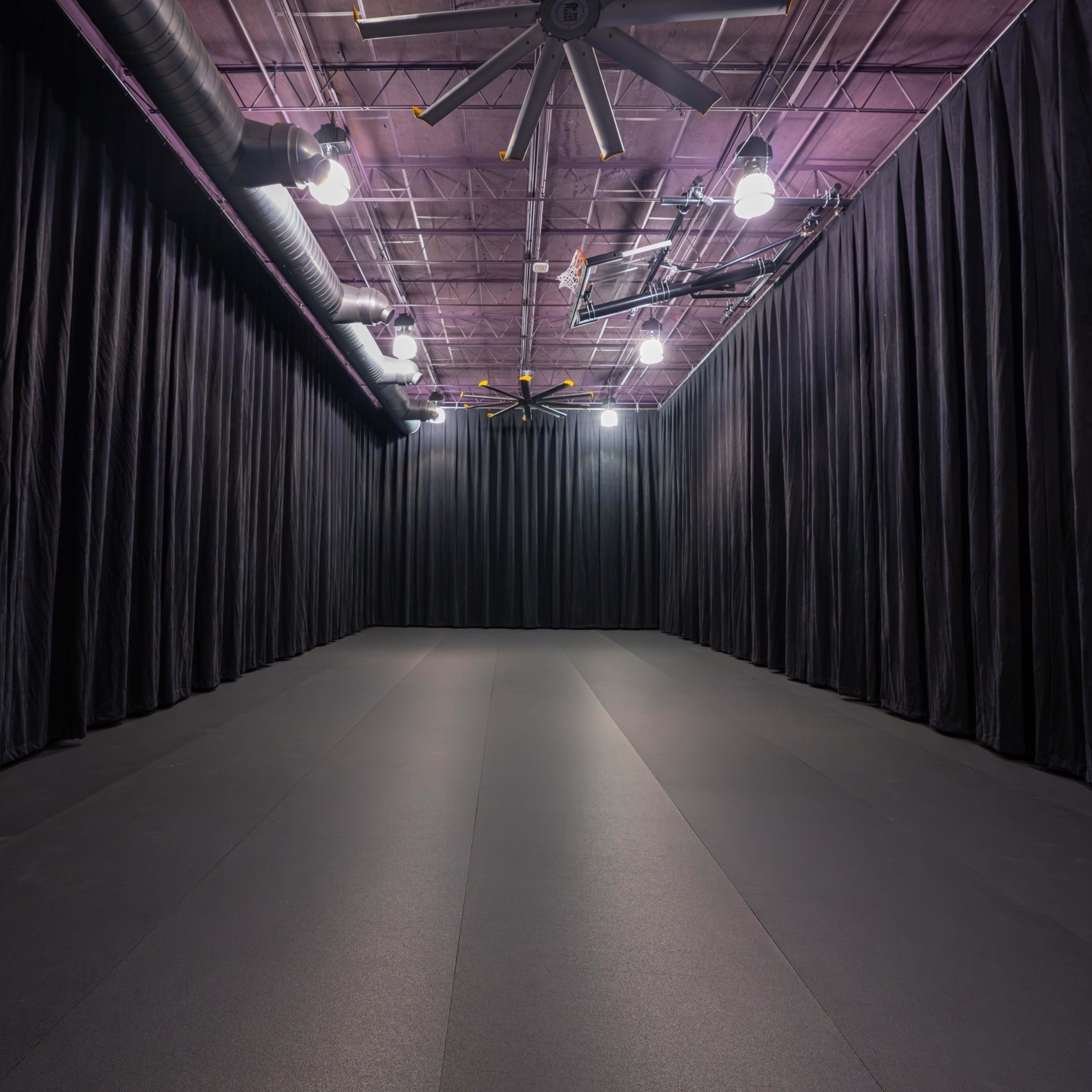 An empty, dimly lit room with black curtains lining the walls and a smooth, dark floor.