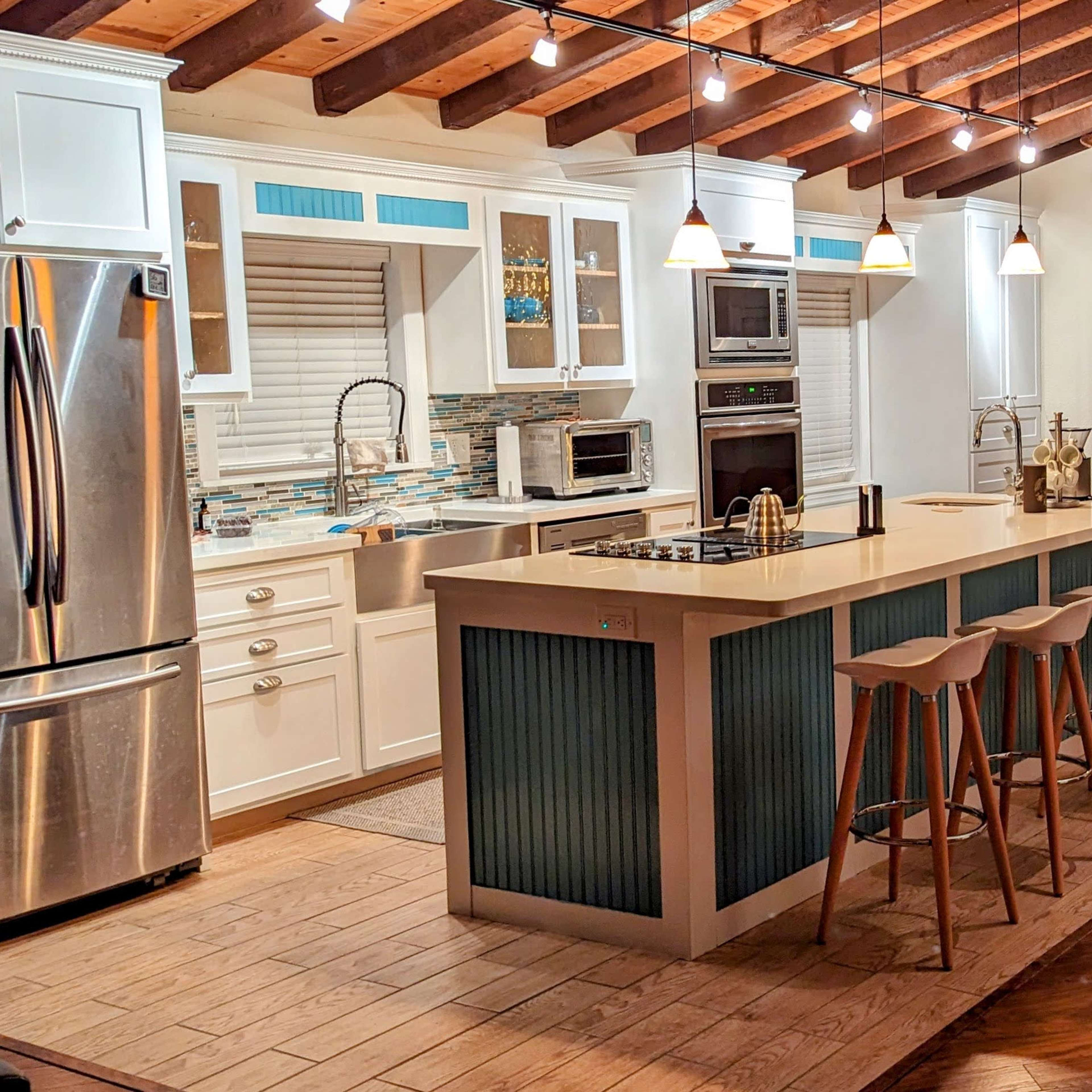 A modern kitchen with a central island and seating, adjacent to a living area featuring a leather couch and wooden flooring.