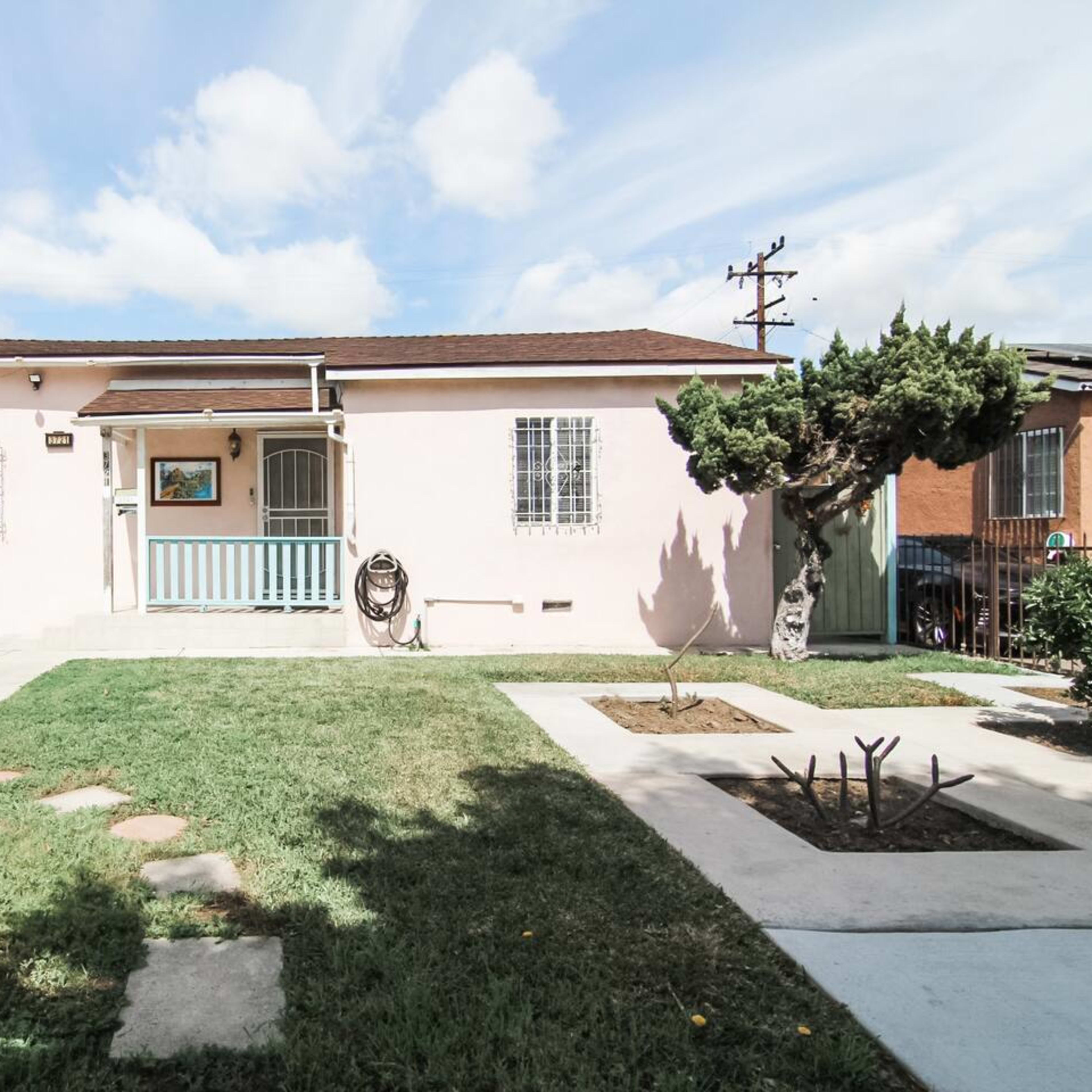 A single-story pink house with a front porch and a neatly maintained lawn is visible, flanked by two other residential buildings.