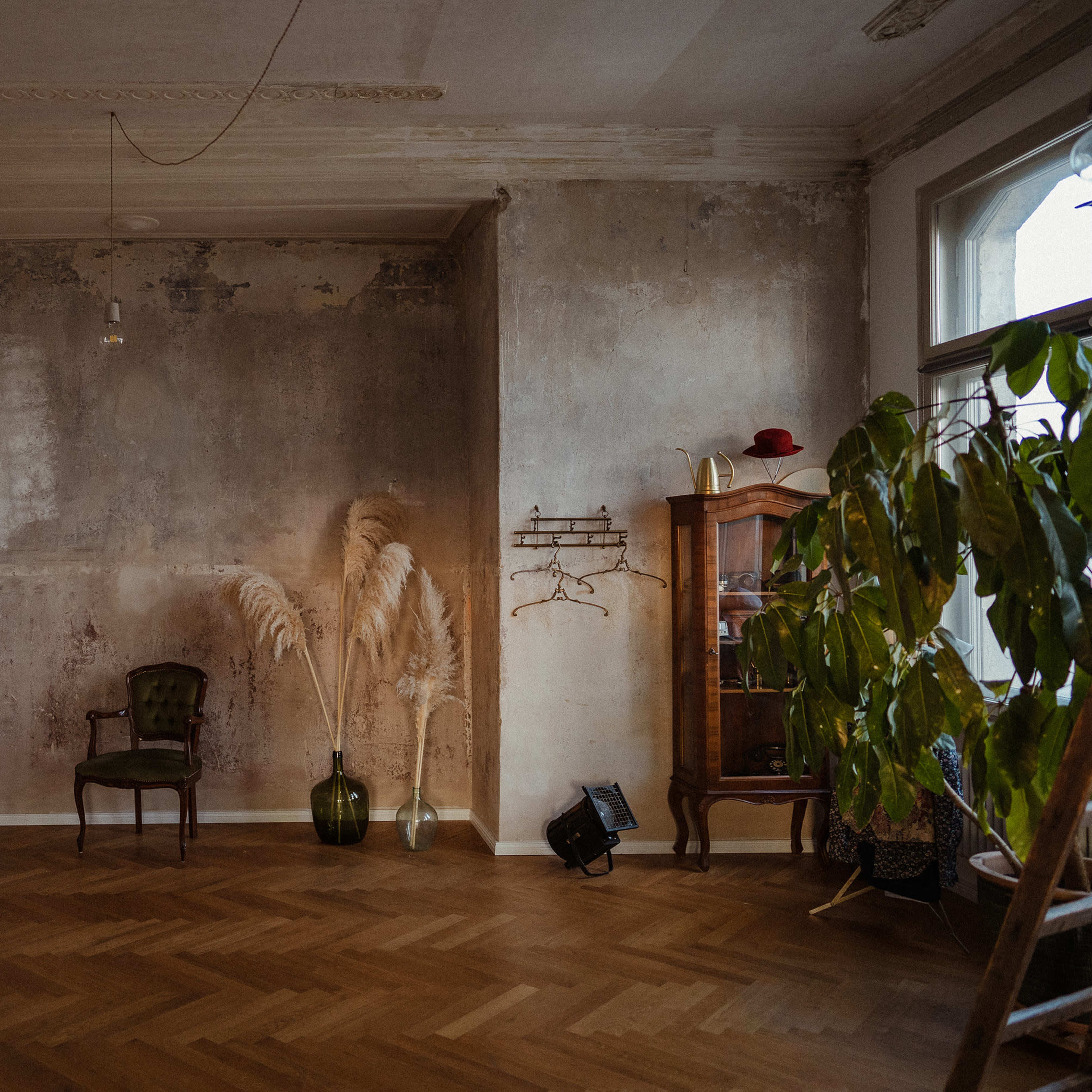 A spacious room with a vintage chair, a coat rack, a tall plant, and a wooden cabinet against a textured wall.