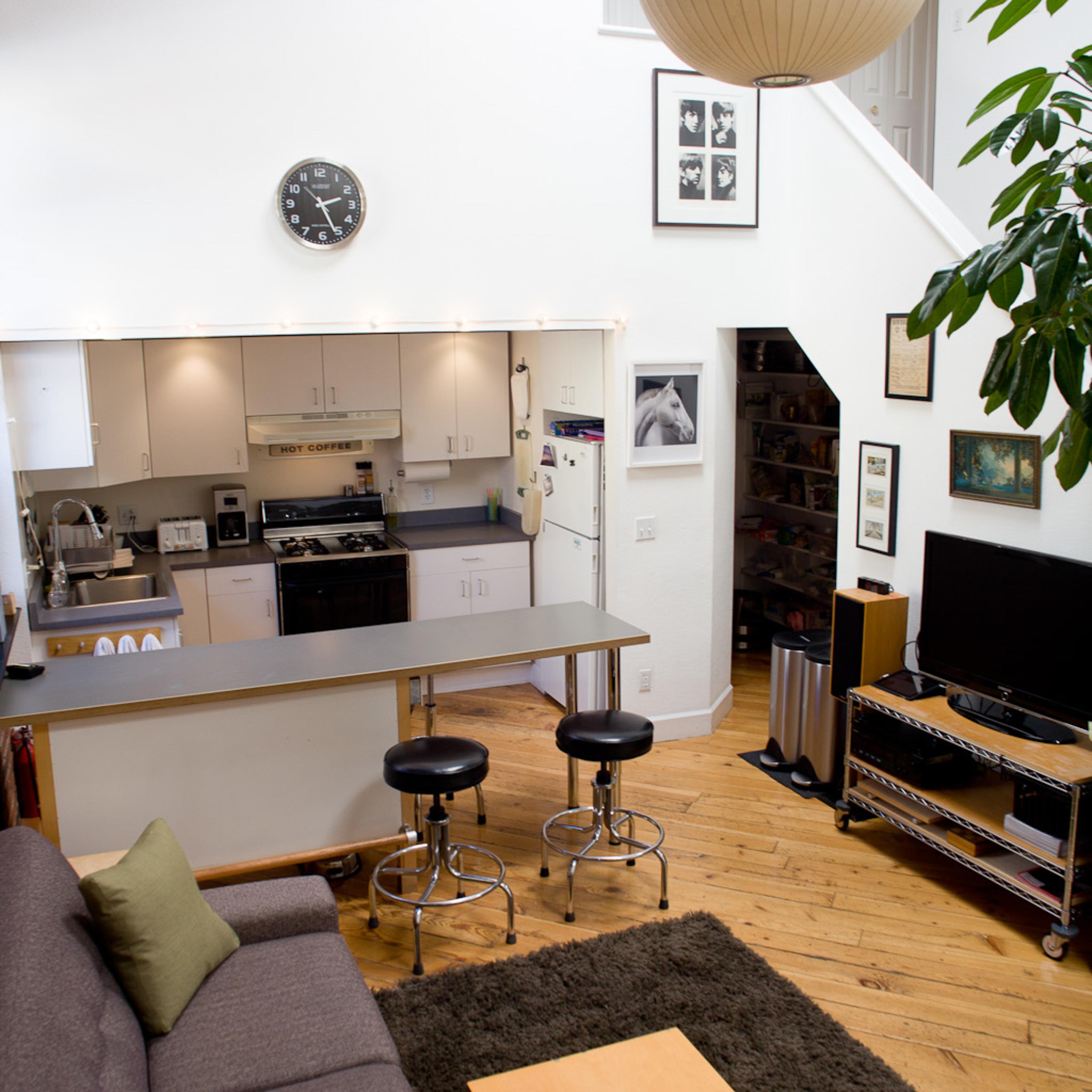 A modern open-concept living space with a kitchen, dining area, and living room, featuring a gray sofa, wooden floor, and a large pendant light.