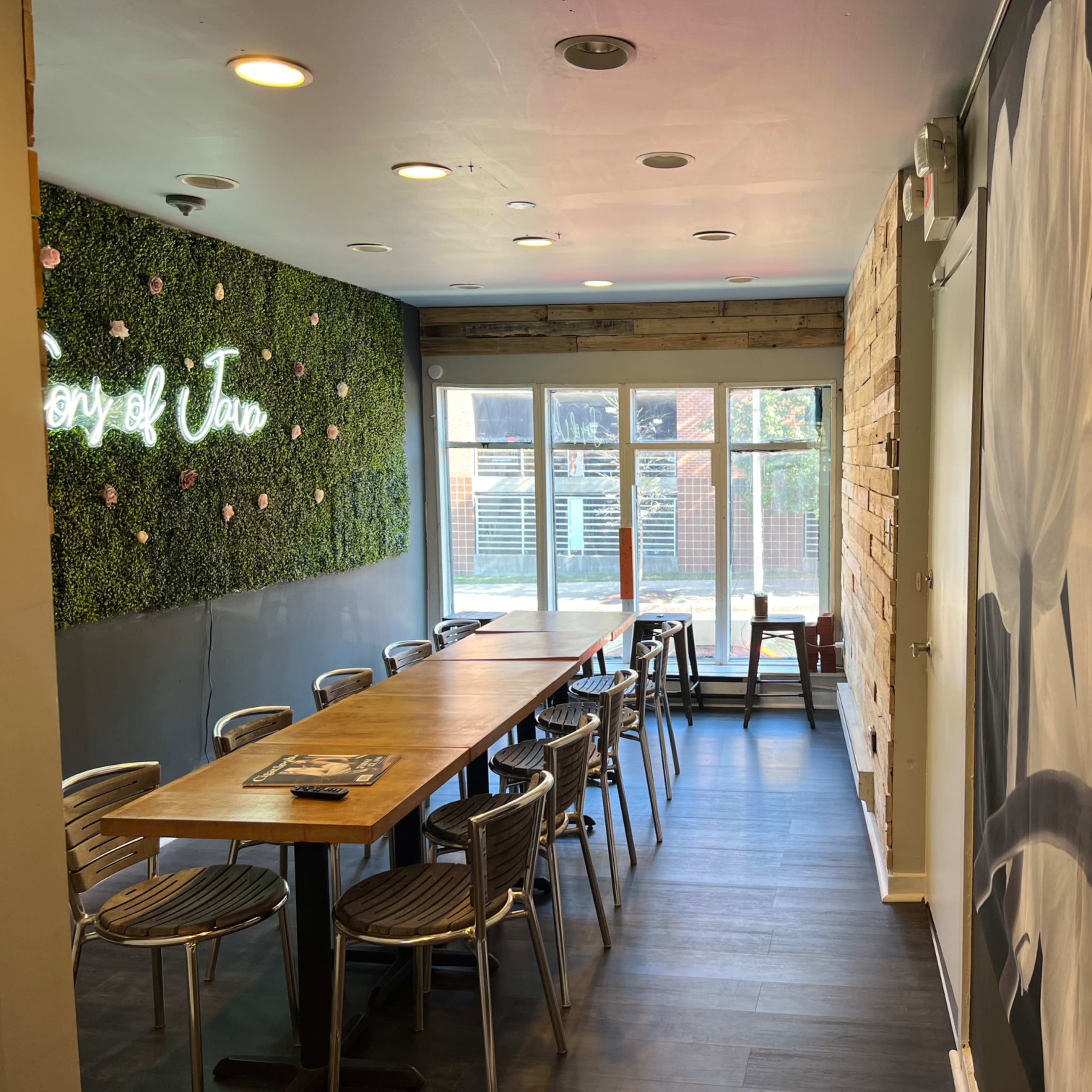 A dining area with a long wooden table and metal chairs, decorated with a green wall of plants on one side and large flower artwork on another.