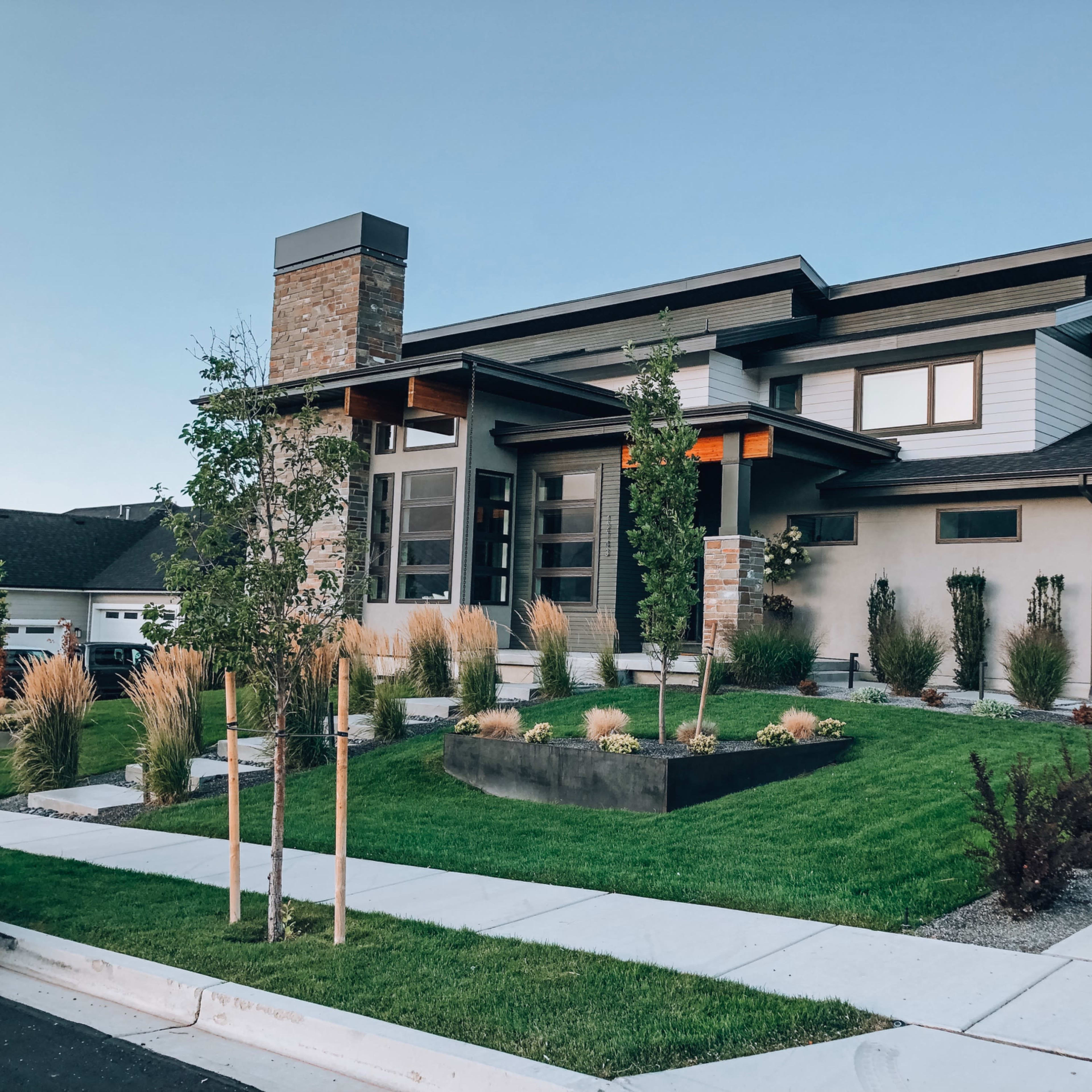 A modern house features a combination of stone and wood elements, with a landscaped yard and a three-car garage.