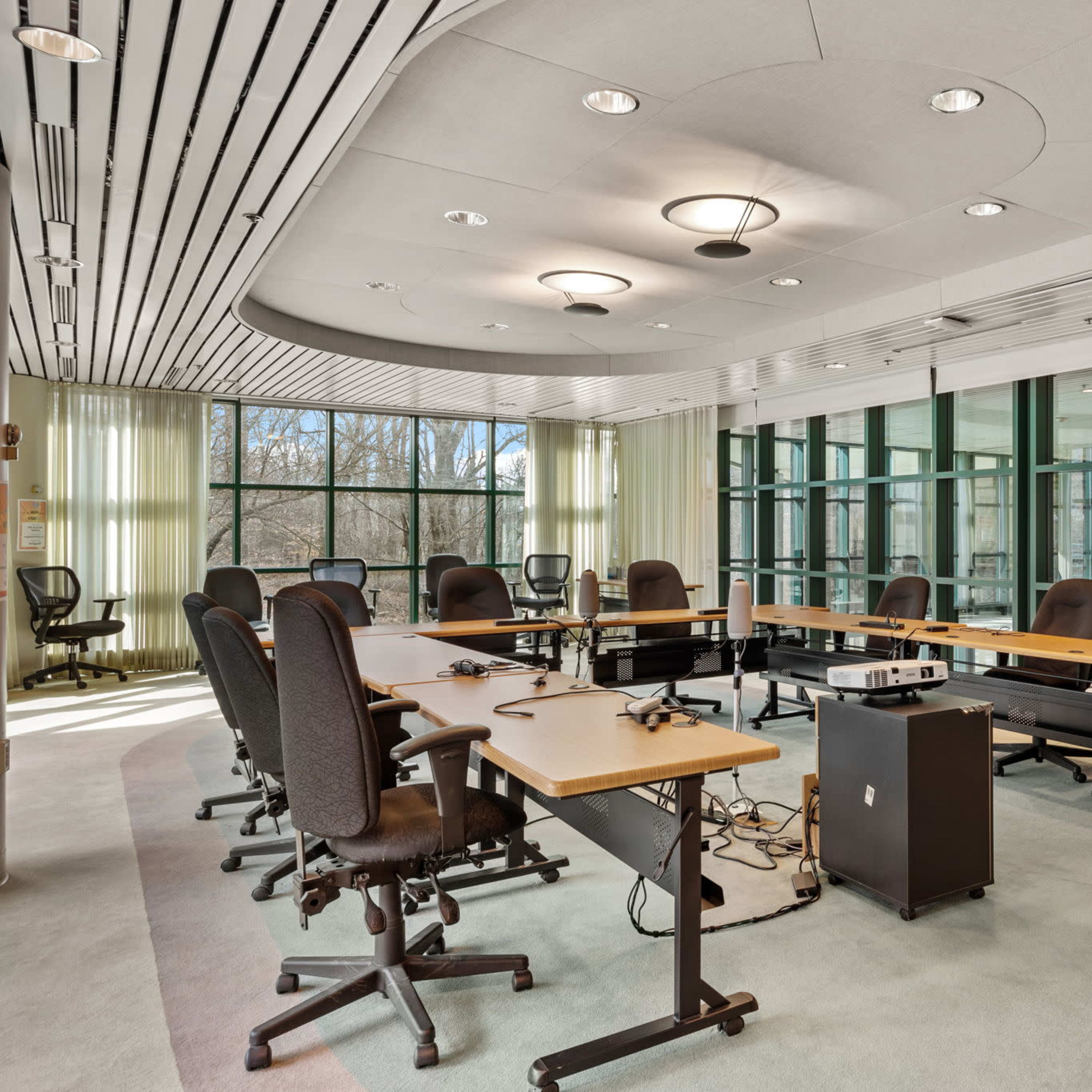 A modern conference room features a circular table surrounded by ergonomic chairs and large windows.