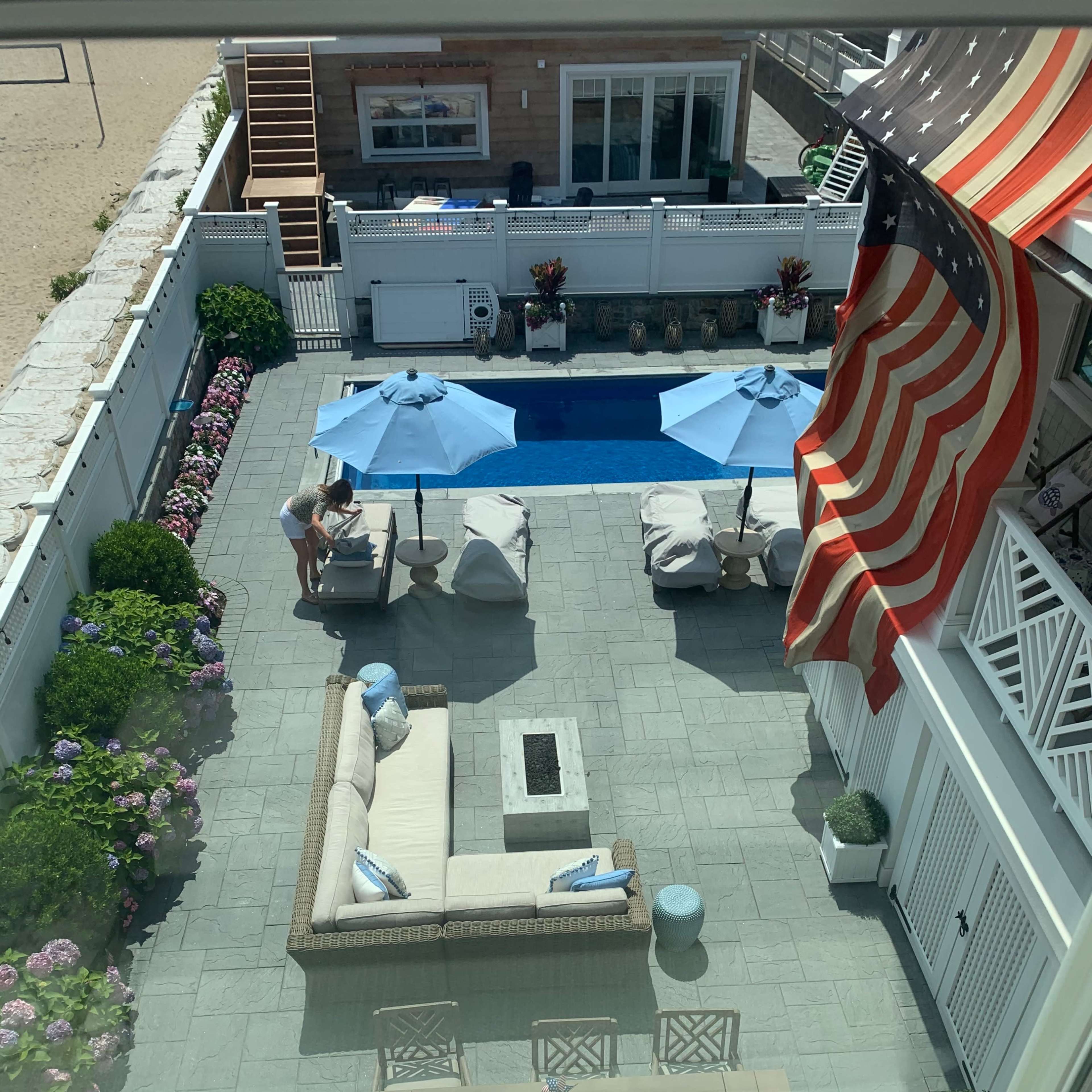 A backyard patio with a pool, lounge chairs, an outdoor sofa, and an American flag hanging above.