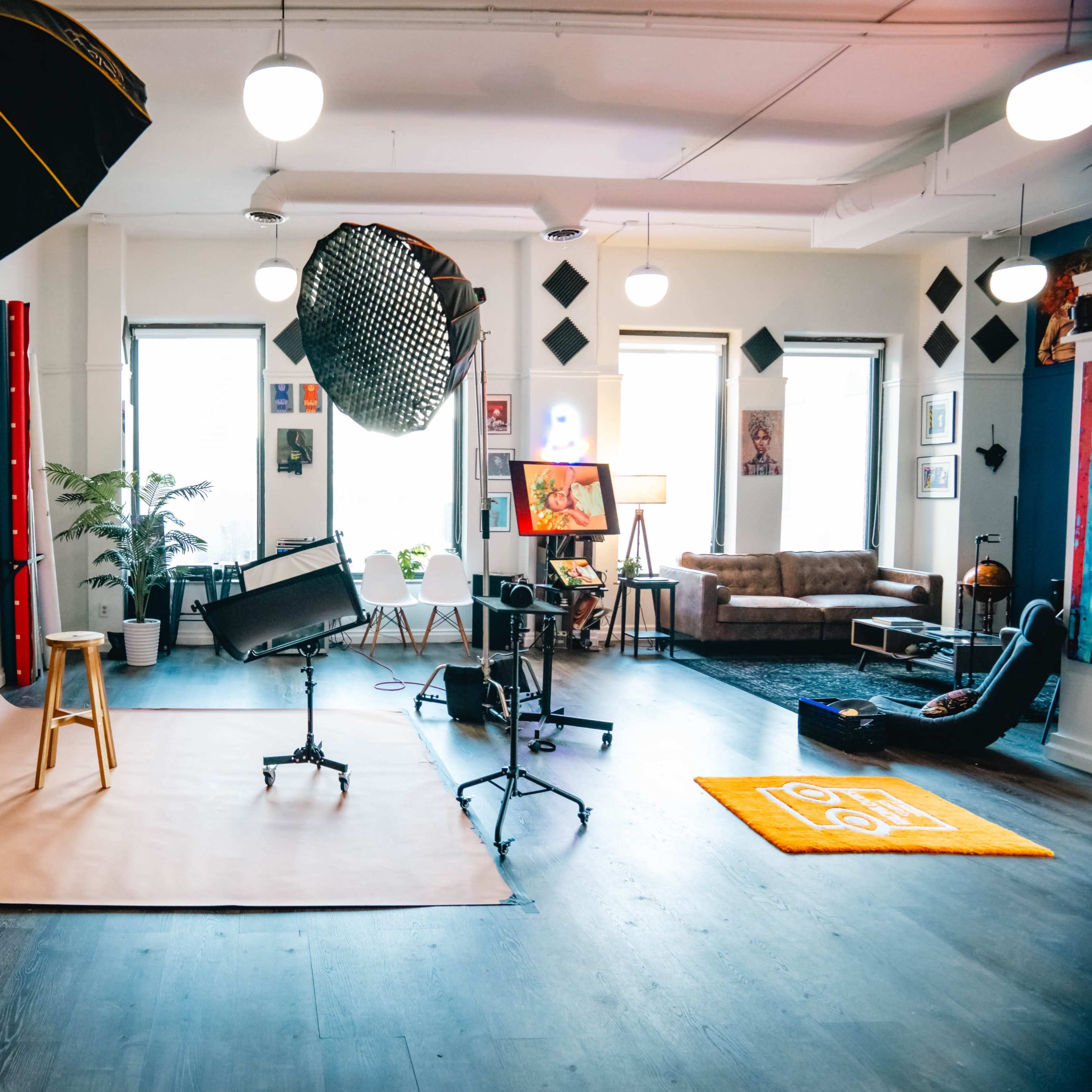 A well-equipped photography studio featuring softboxes, a backdrop, a stool, and various artwork displayed on the walls.