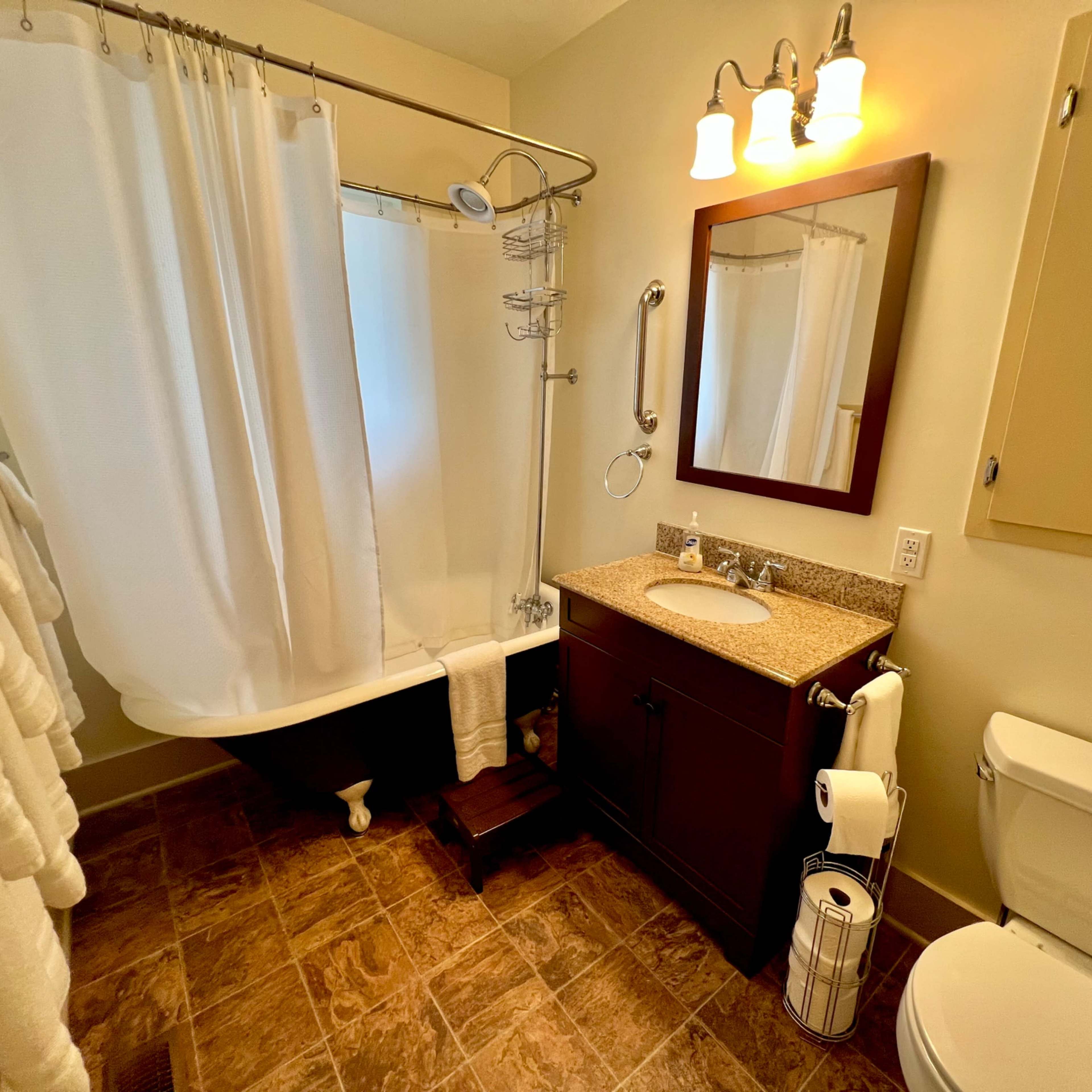 The bathroom features a shower-tub combination, a sink with a granite countertop, a mirror, and a toilet, along with two towels hanging on a rack.