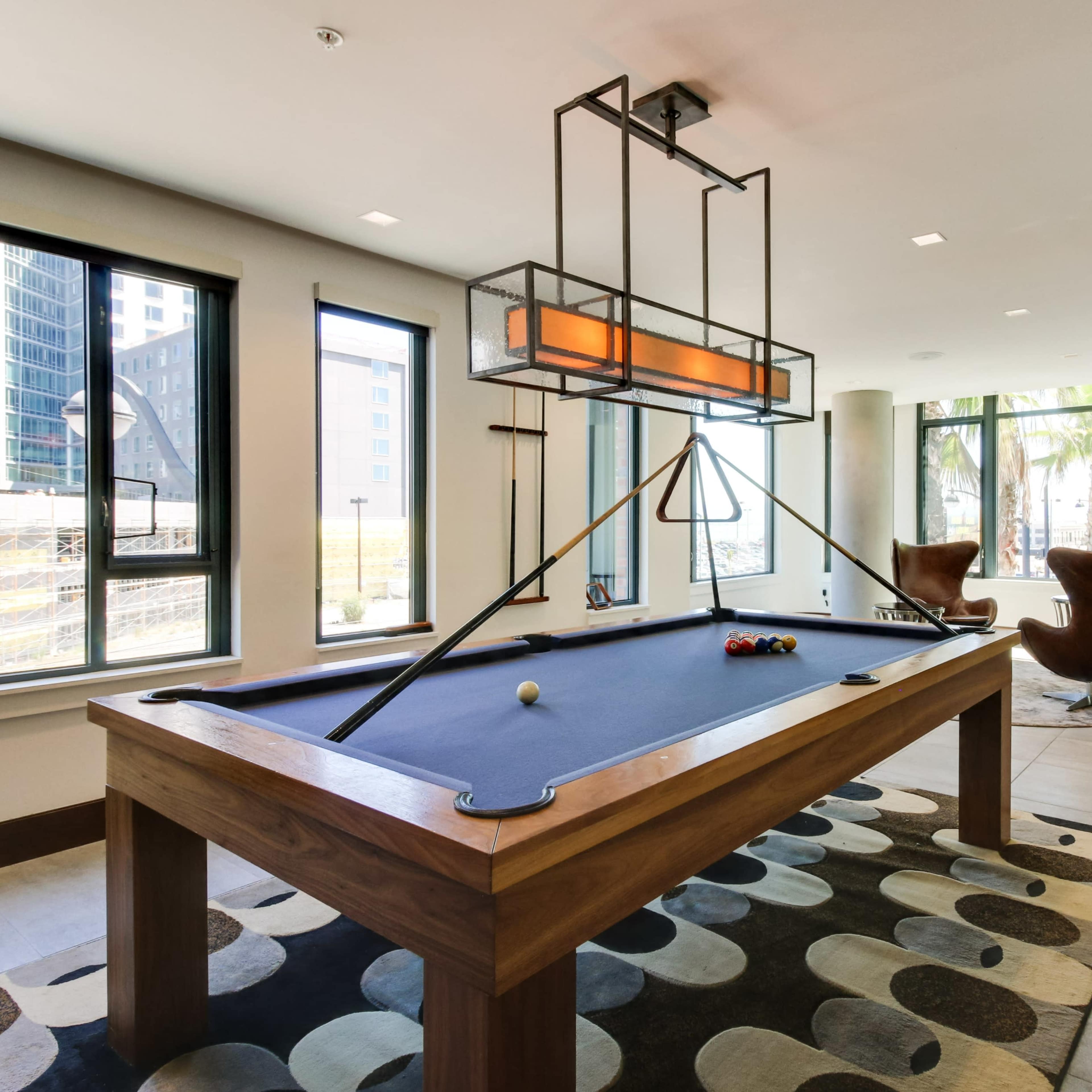 A modern indoor space featuring a pool table, large windows, and contemporary seating arrangements.