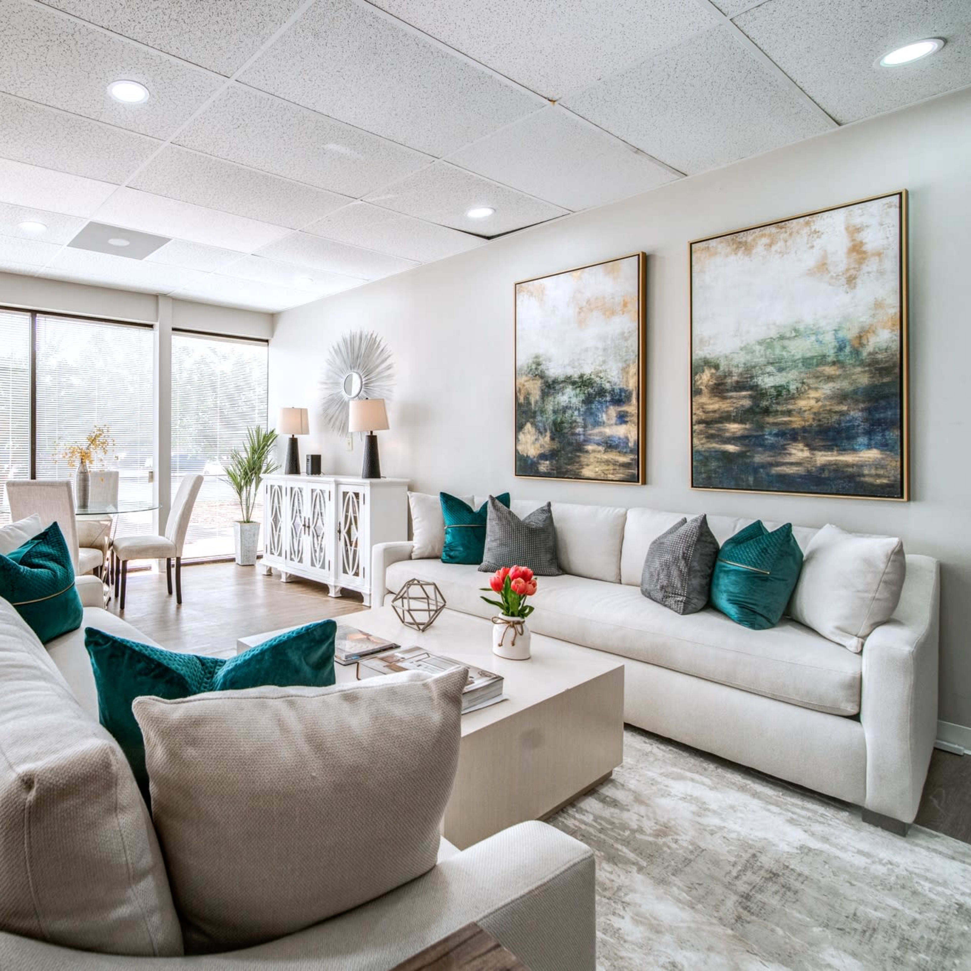 A modern waiting area with two sofas, decorative art on the walls, and floor-to-ceiling windows letting in natural light.