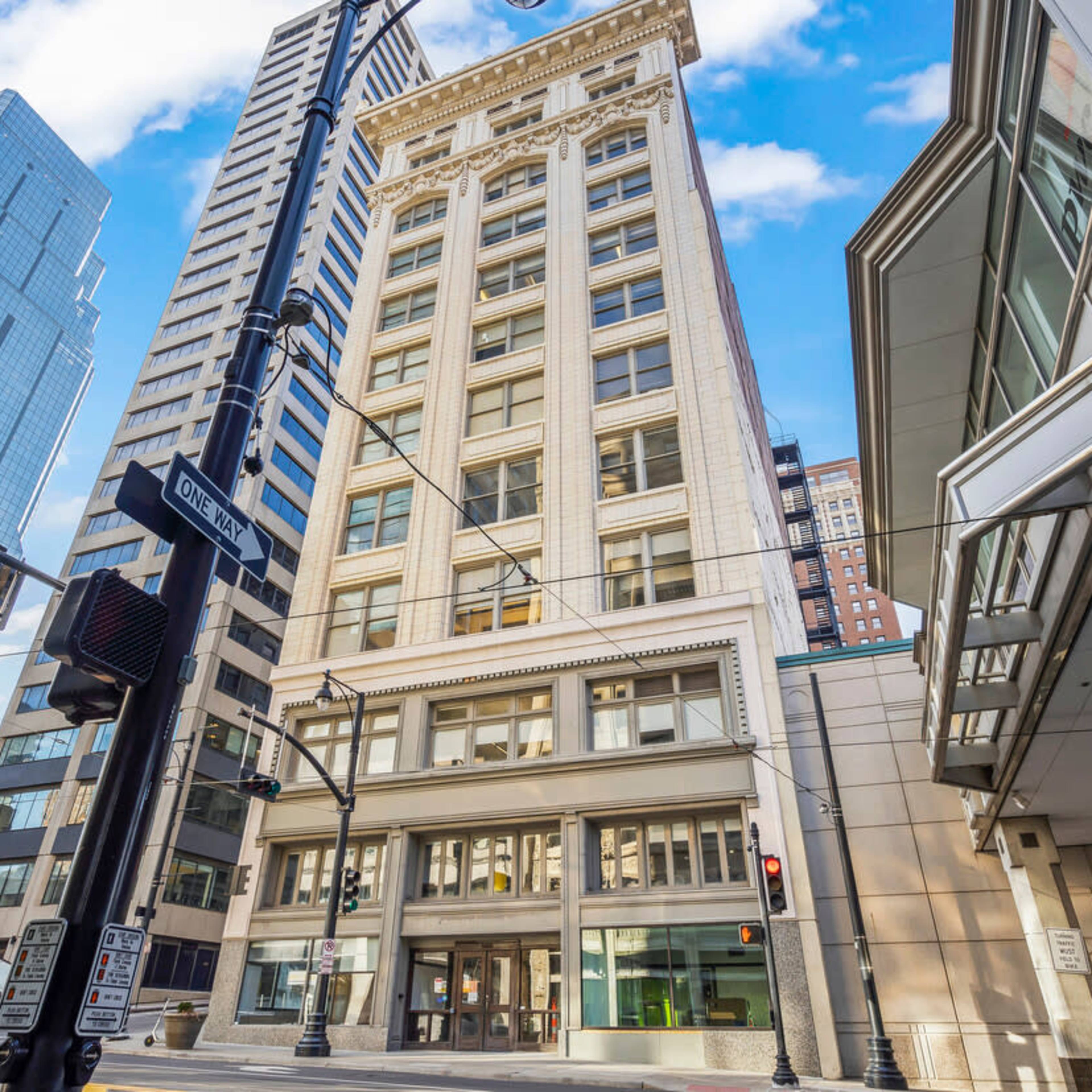 A tall building with a classic facade positioned at the intersection of two city streets, surrounded by modern skyscrapers.