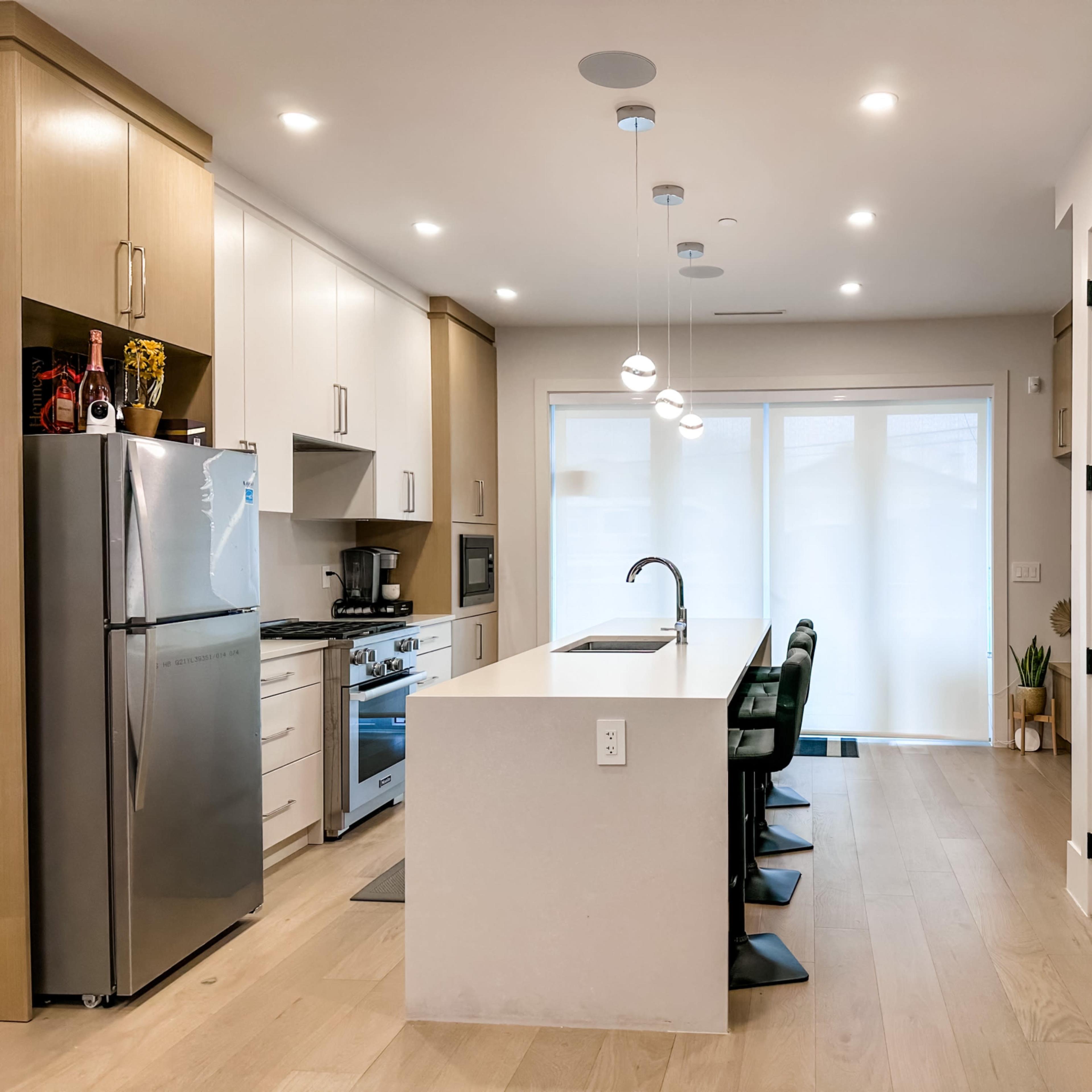 A modern kitchen features stainless steel appliances, a central island with seating, and large windows that provide natural light.