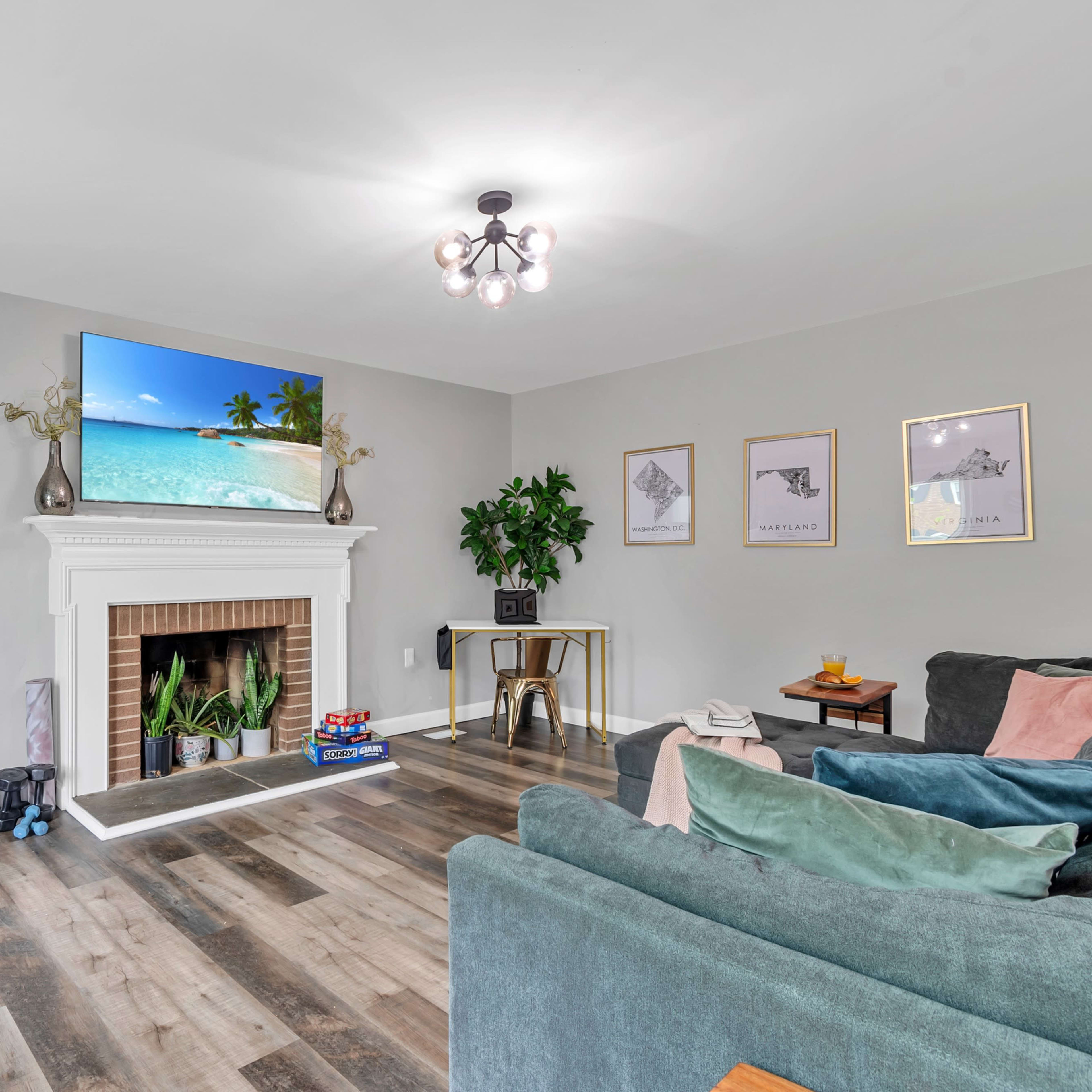 The living room features a TV mounted above a fireplace, surrounded by plants and decorative artwork on the walls.