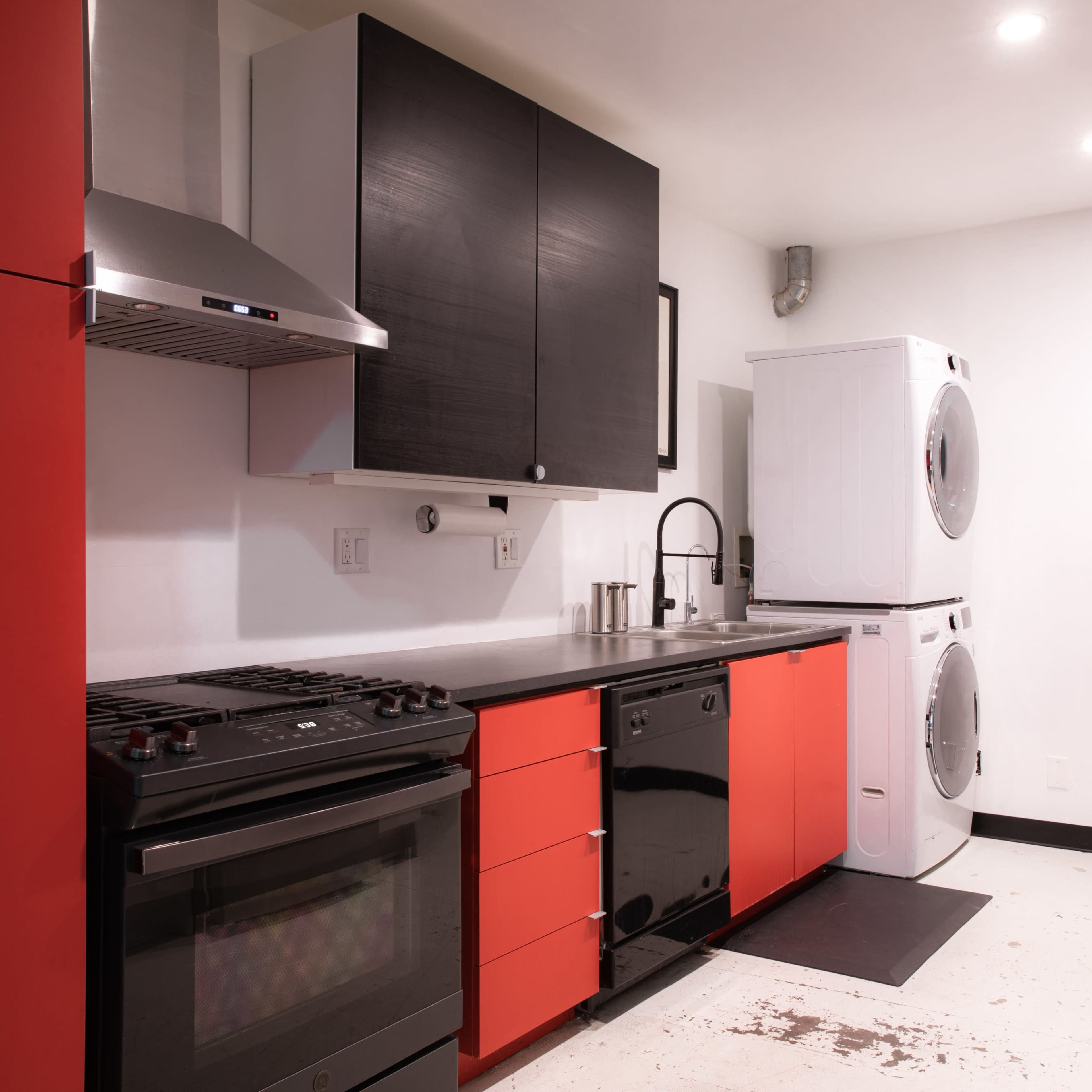A modern kitchen with black and red cabinetry, a stainless steel stove, and a stacked washer and dryer.