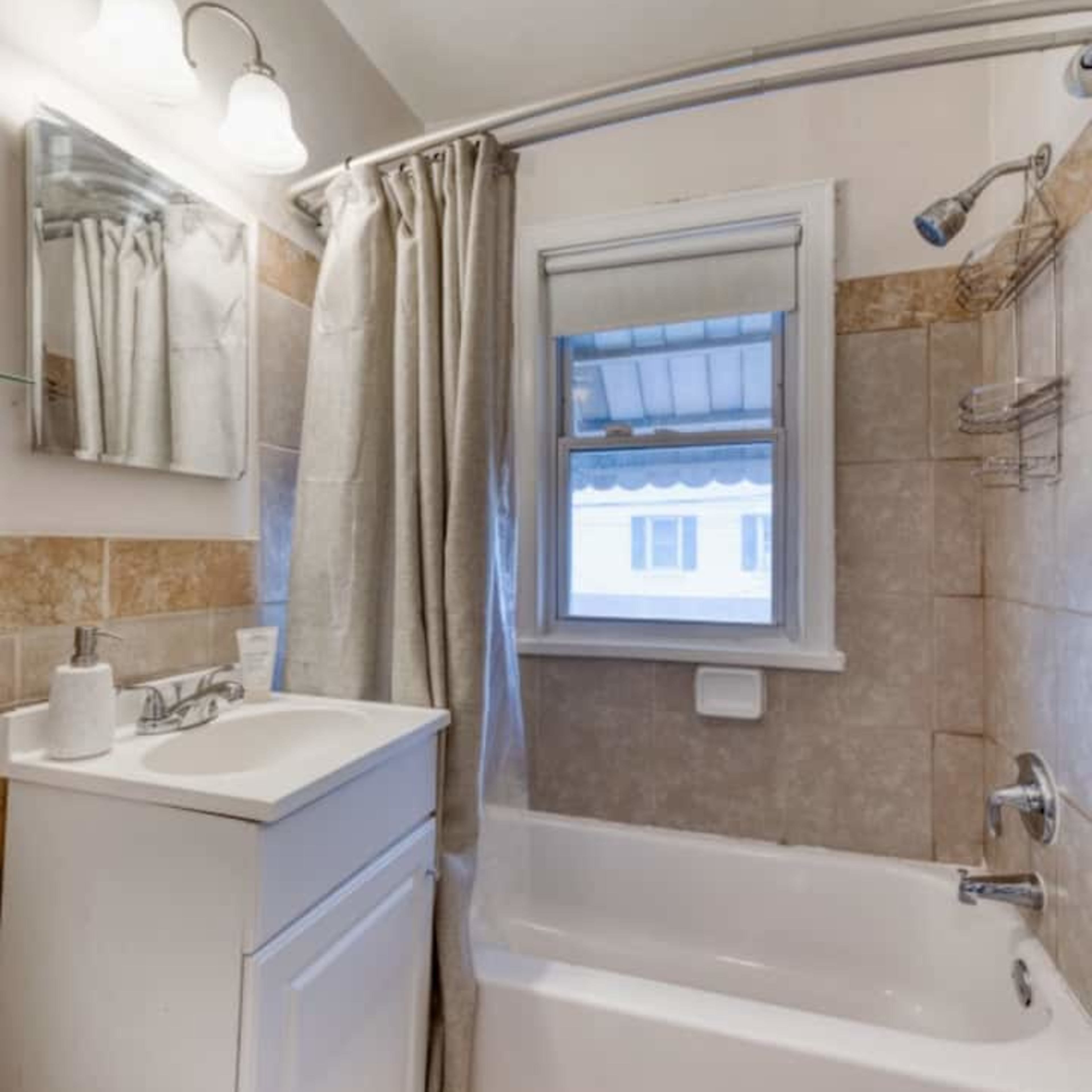 A compact bathroom with a bathtub, a shower curtain, a sink with a cabinet, and a mirror above the sink.