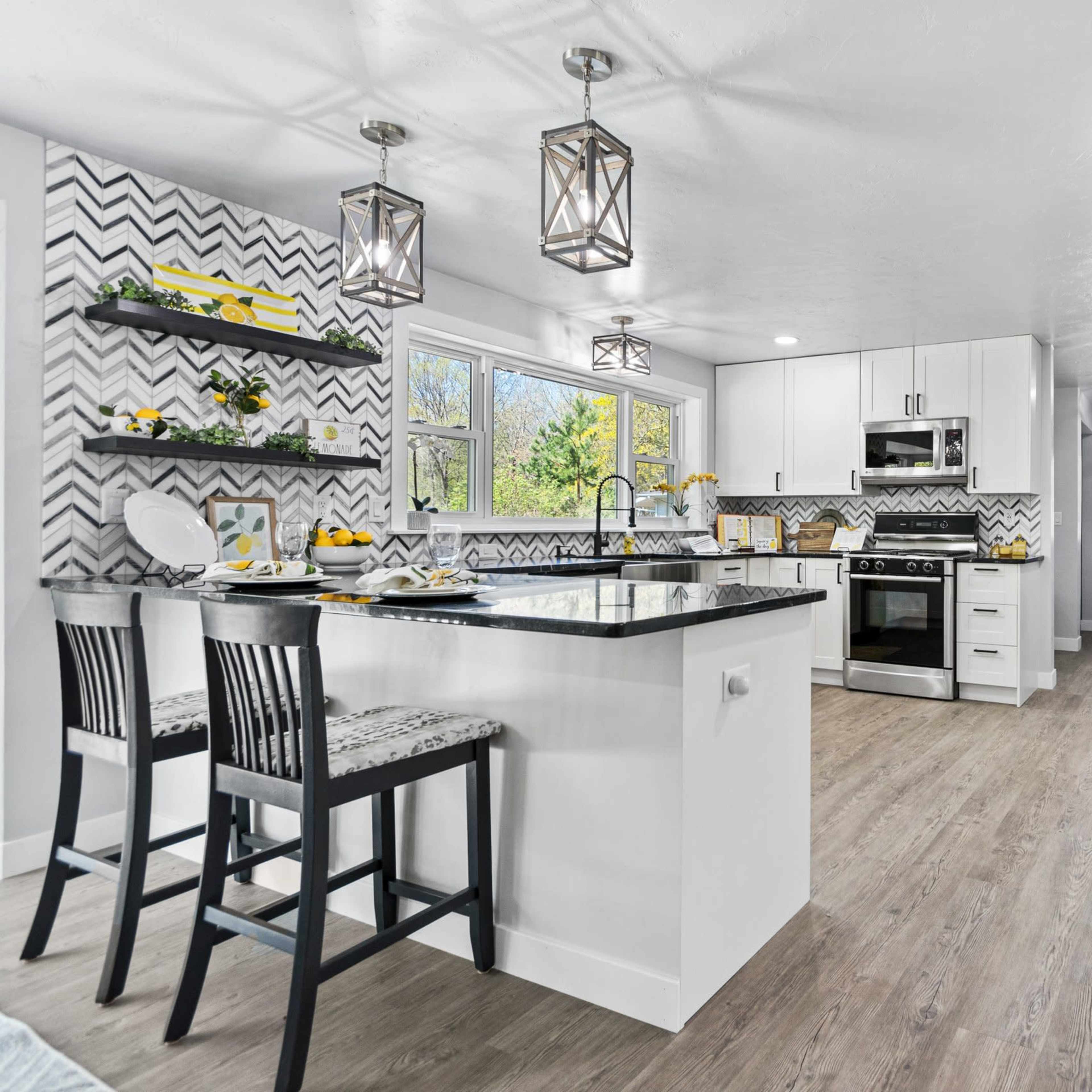 A modern kitchen with a white and grey color scheme, featuring an island with black countertops, bar stools, and patterned backsplash.