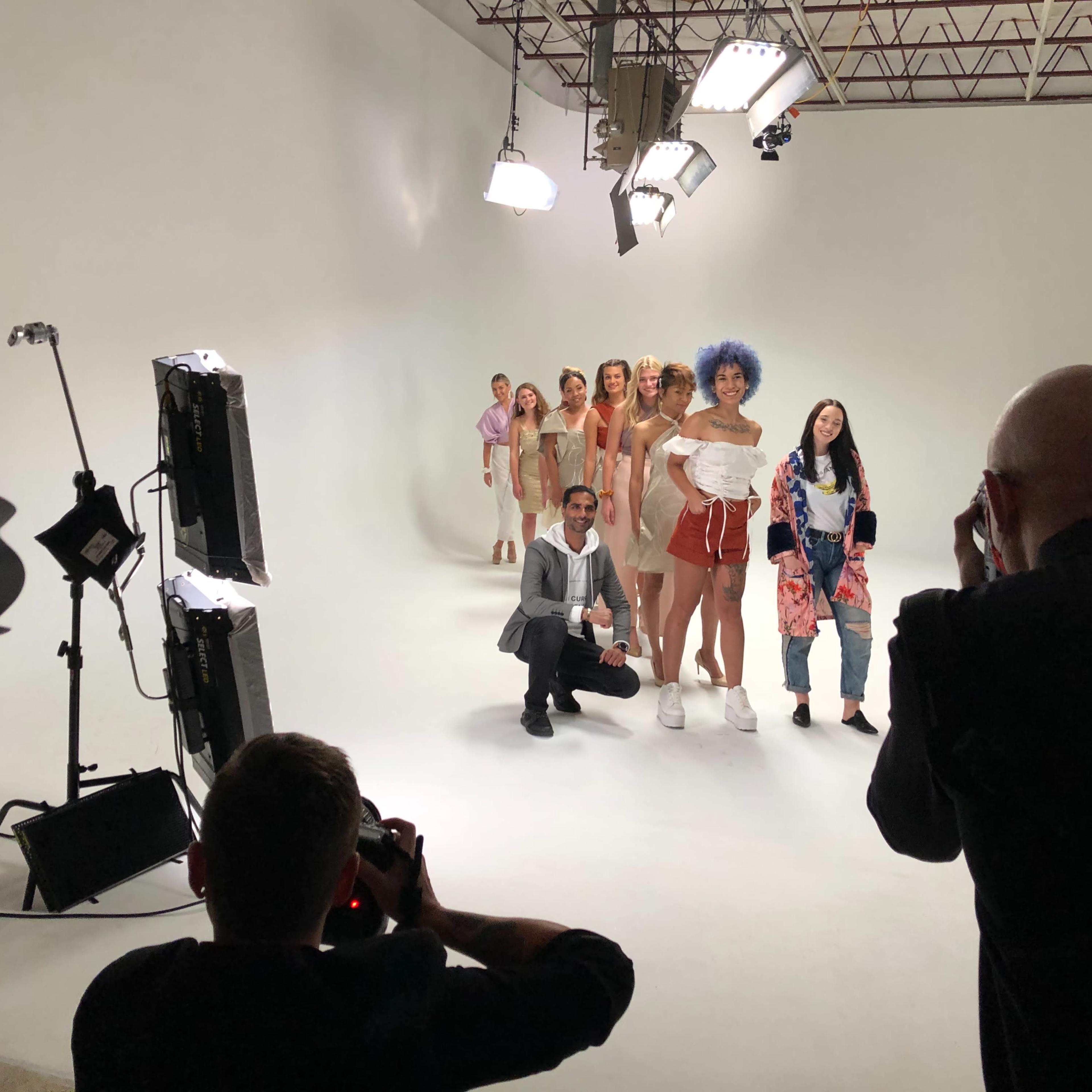 A group of models poses for a photo shoot in a studio with bright lighting and a seamless white backdrop.