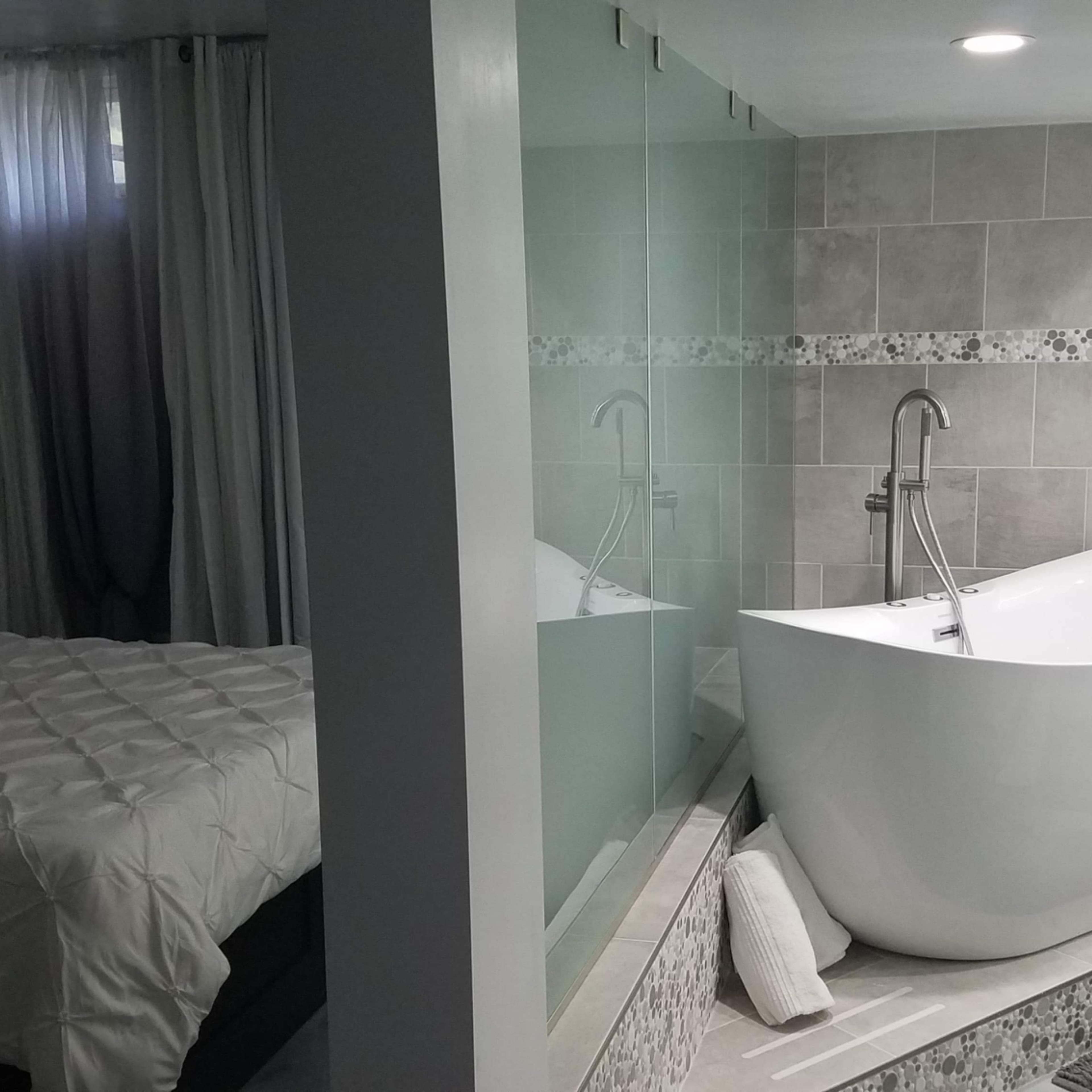 A modern bathroom with a freestanding bathtub and a separate area featuring a bed and curtains.