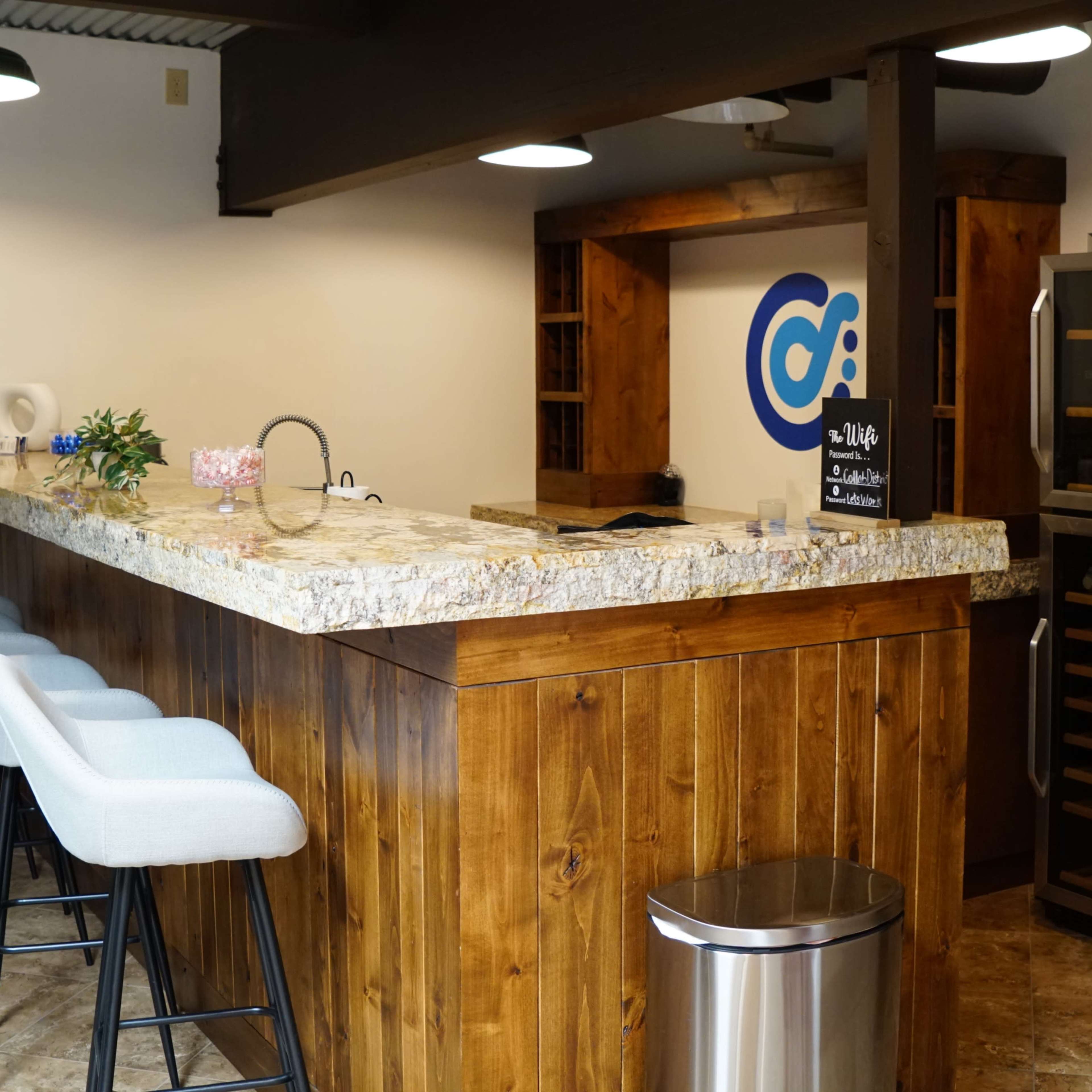 A minimalist bar area with a granite countertop, wooden cabinetry, a modern refrigerator, and several bar stools arranged along the counter.