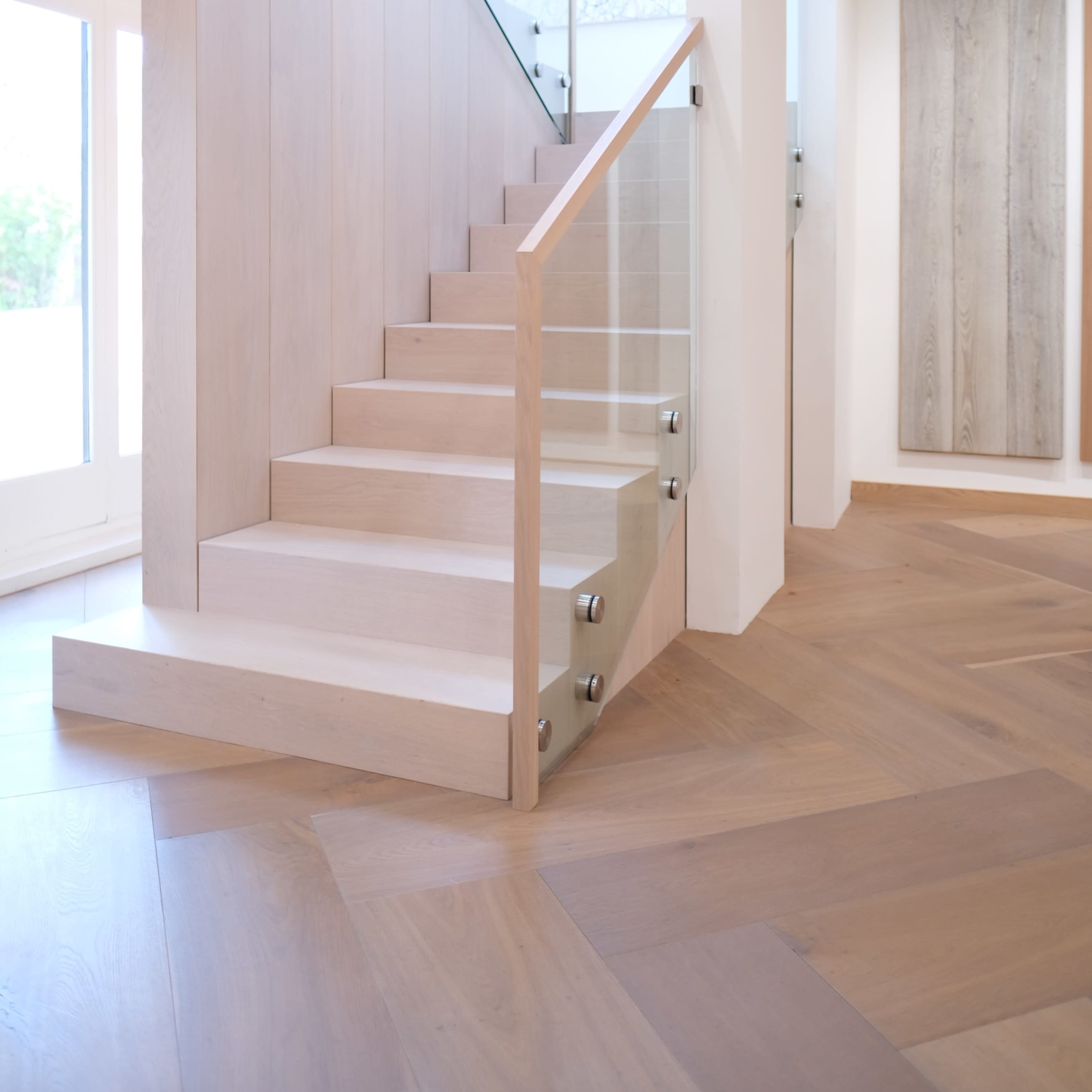 A modern wooden staircase with a glass railing in a brightly lit interior space.